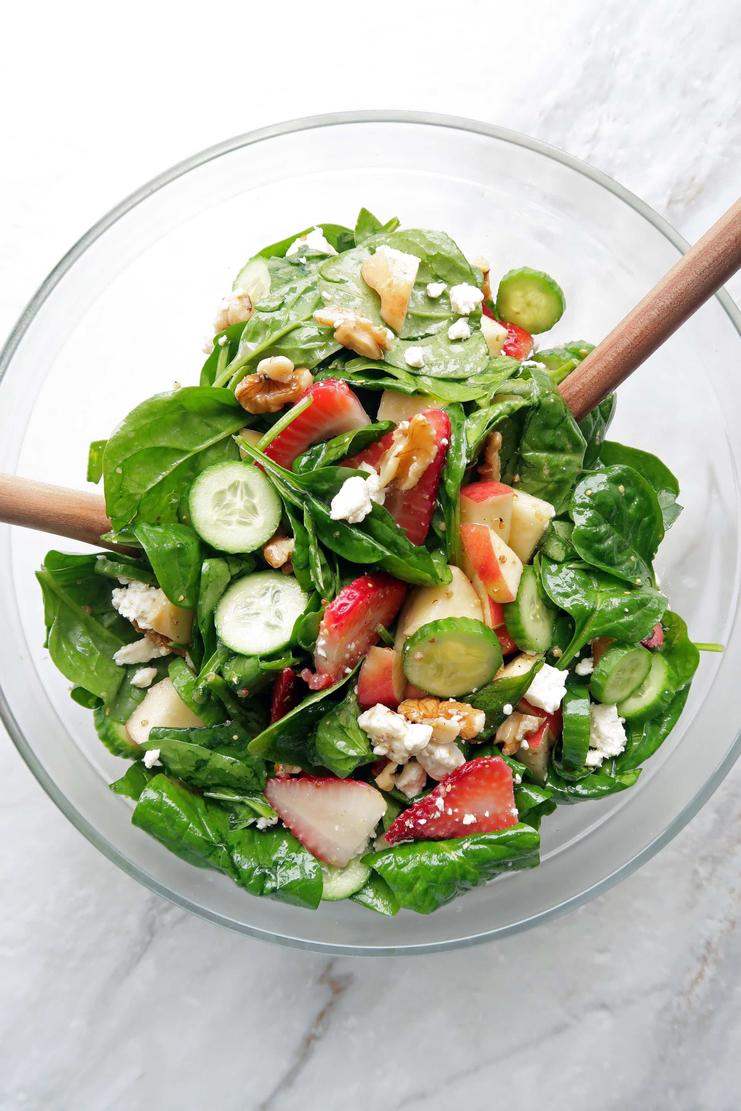 Summer Strawberry Cucumber Spinach Salad with Apple Cider Vinaigrette in a large glass bowl with two wooden spoons.