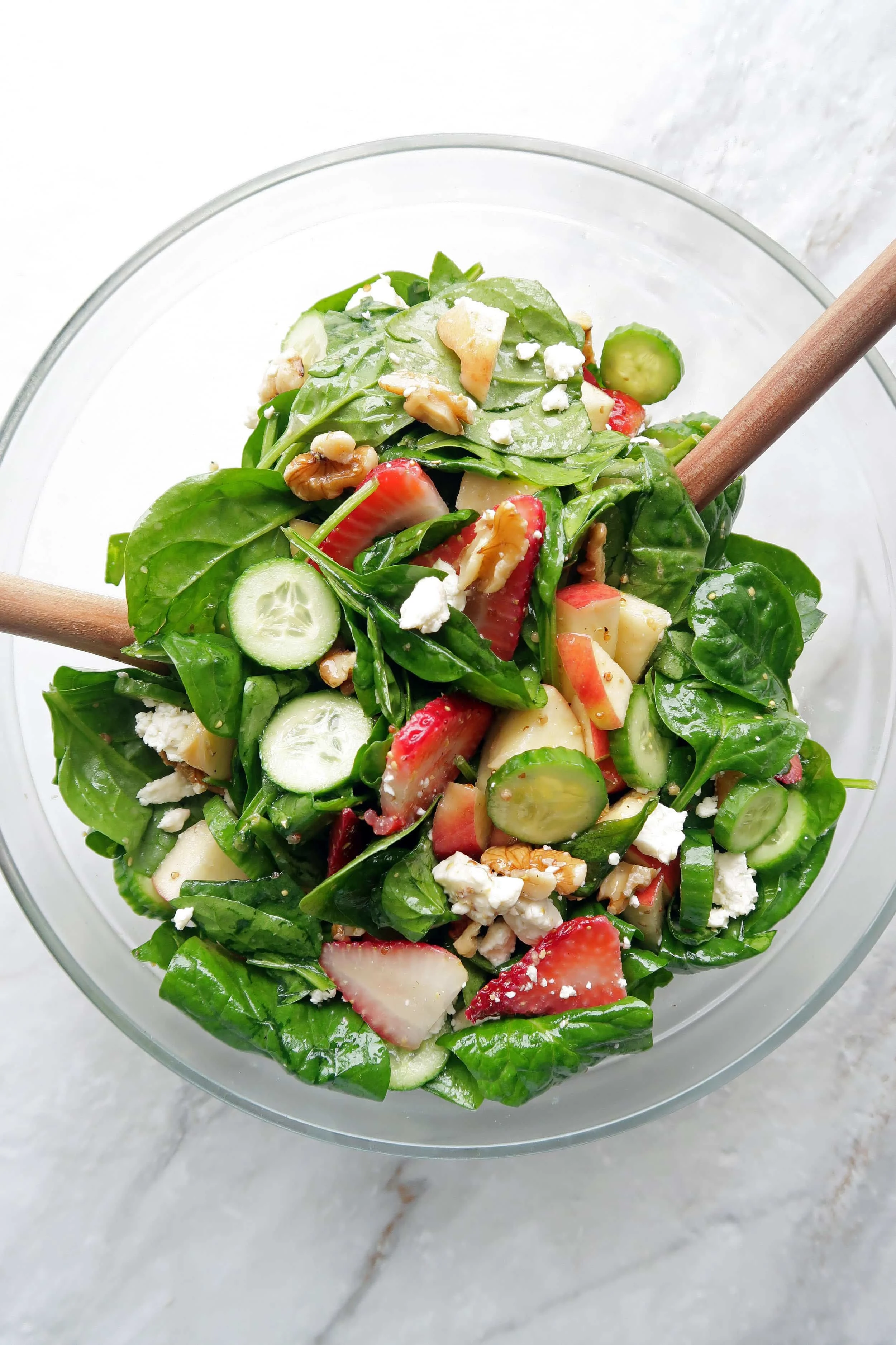 Summer Strawberry Cucumber Spinach Salad with Apple Cider Vinaigrette in a large glass bowl with two wooden spoons.