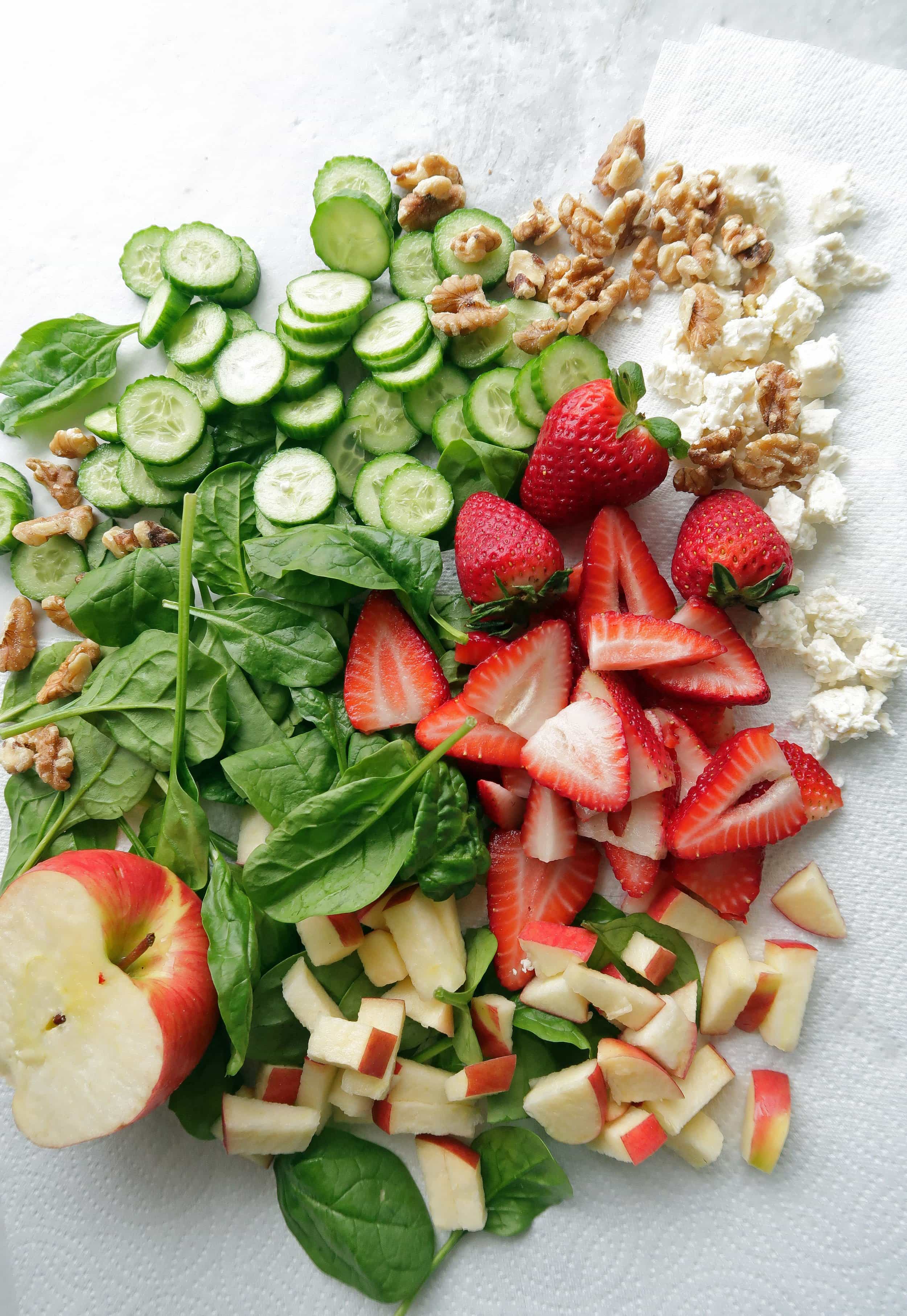 Spinach topped with pieces of apple, strawberry halves, cucumber slices, walnuts, and feta.