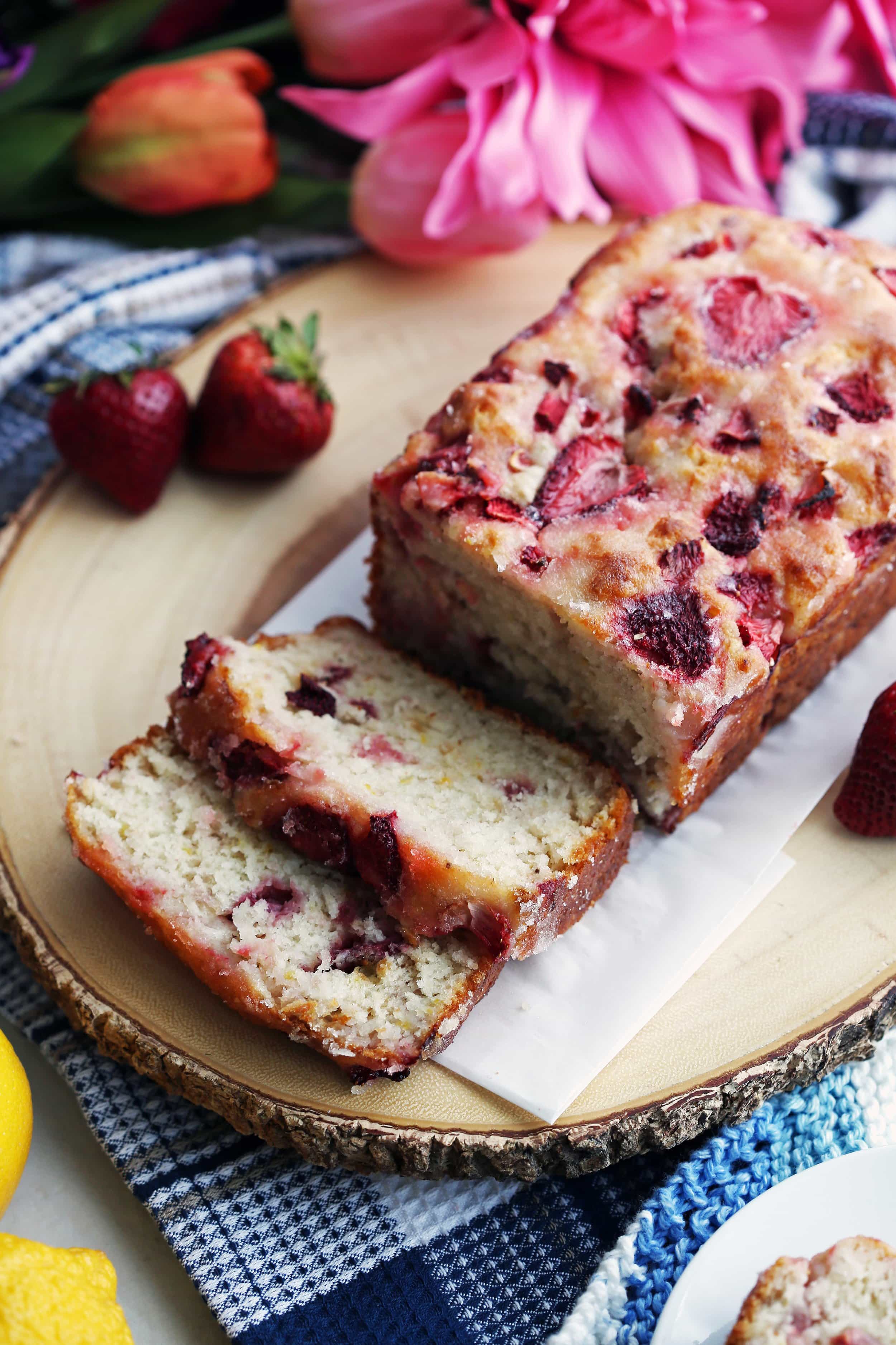 A loaf of Strawberry Lemon Yogurt Quick Bread with two slices cut on a large wooden platter.