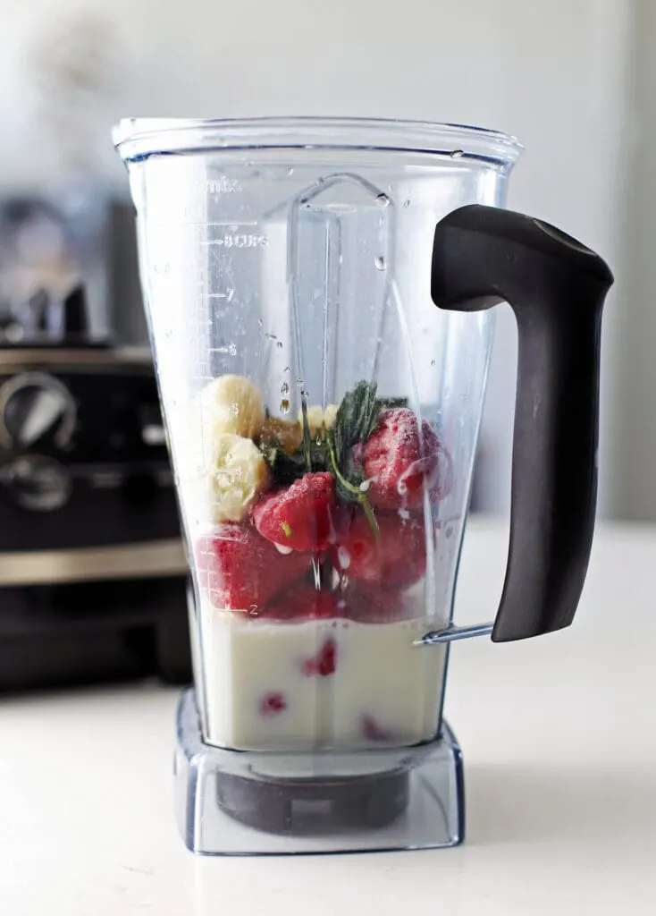 Strawberry smoothie ingredients in a blender container.