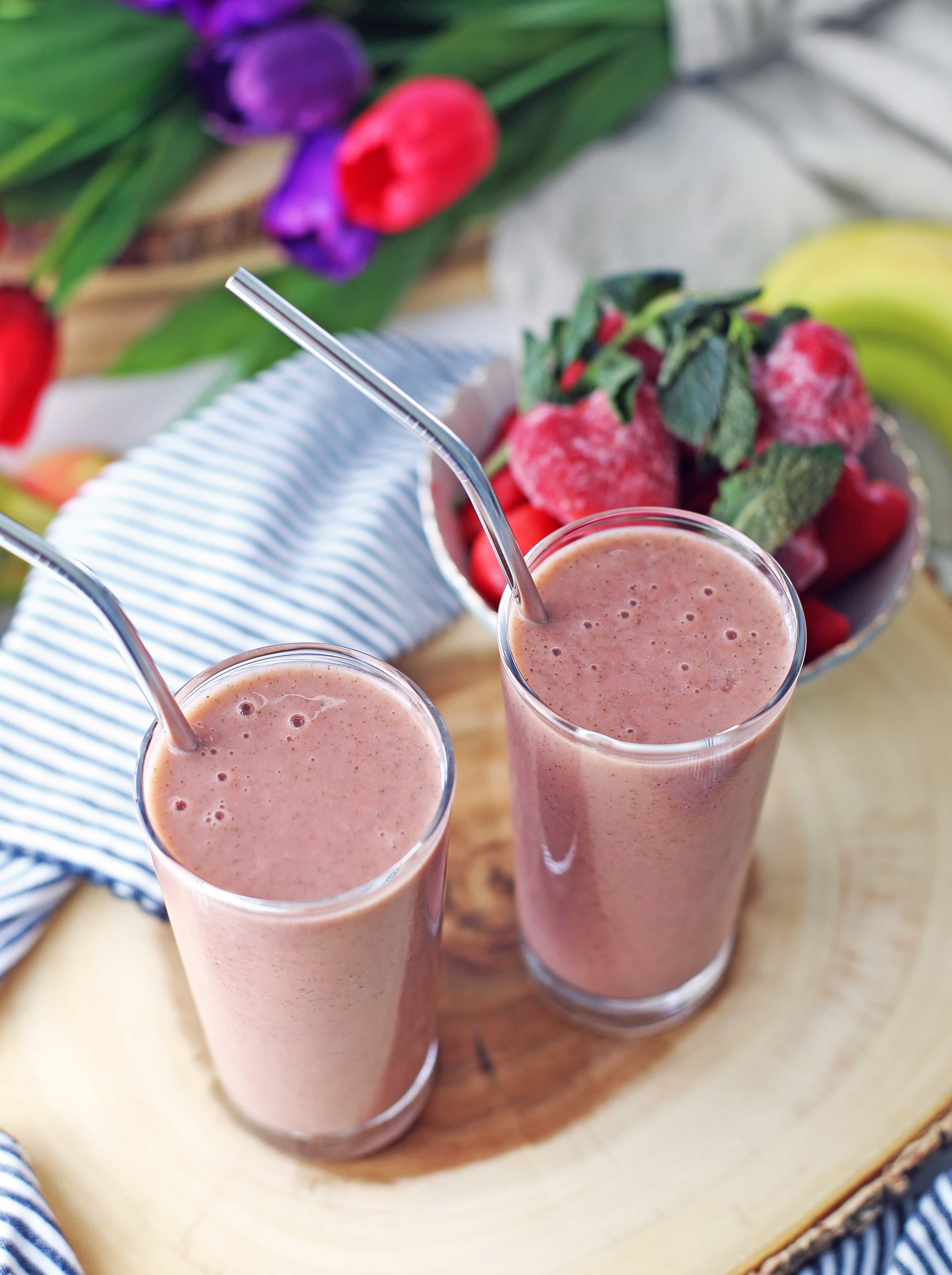 Strawberry mint smoothie in two tall glasses on a wooden platter.