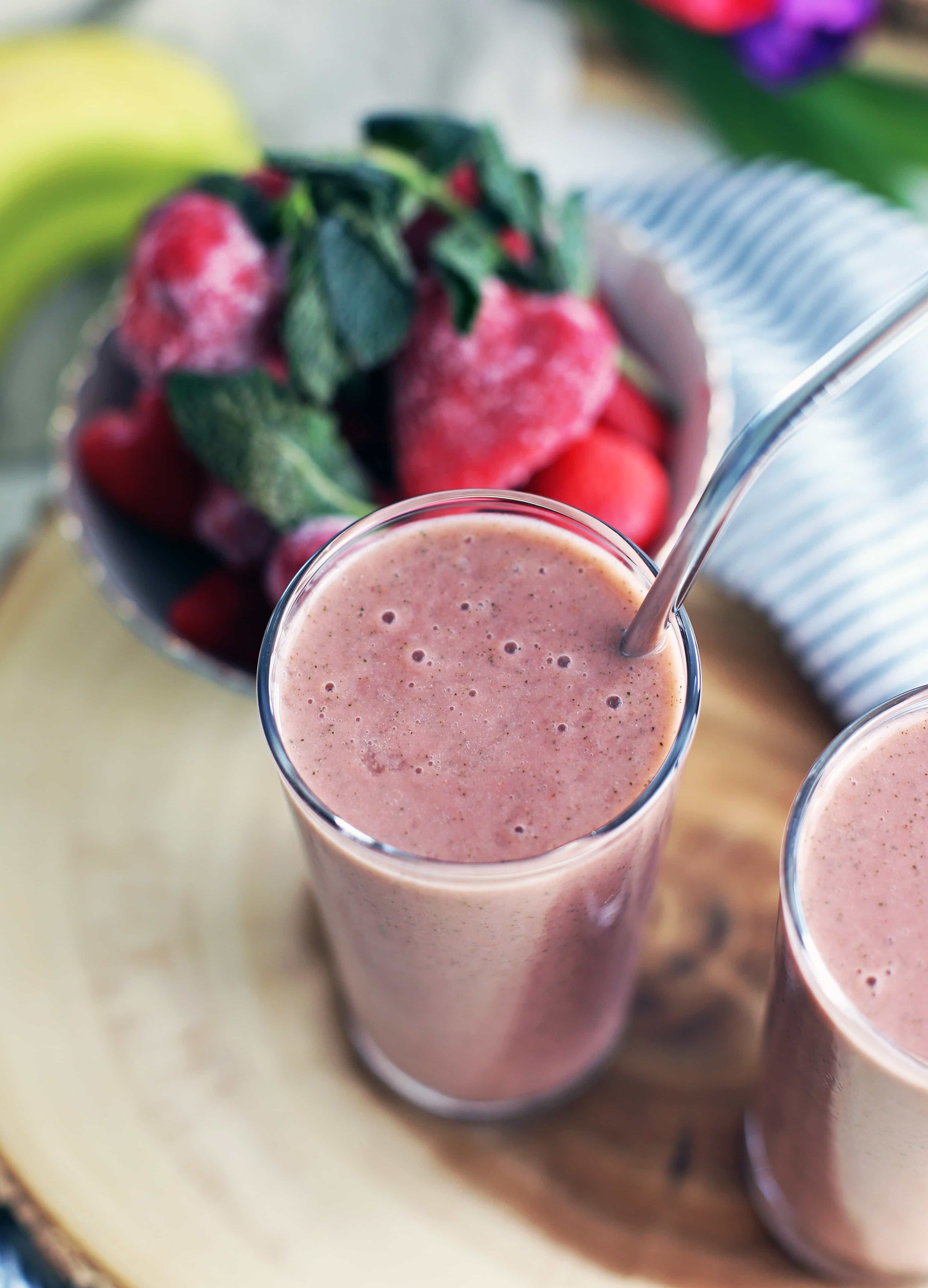 A closeup of a glass containing strawberry mint smoothie with a metal straw.