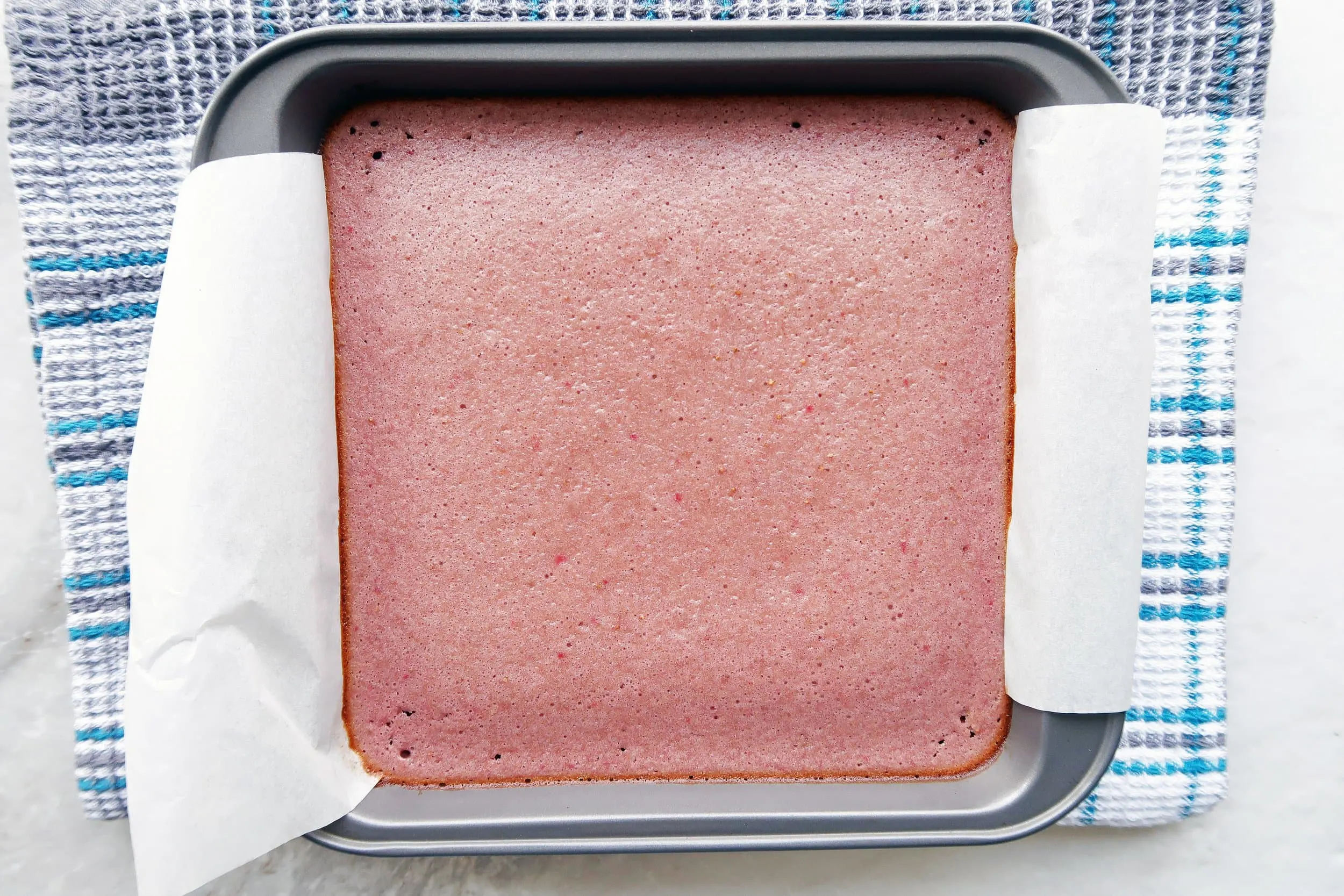 Soft and spongy strawberry layer baked on top of shortbread in a parchment-paper lined baking pan.