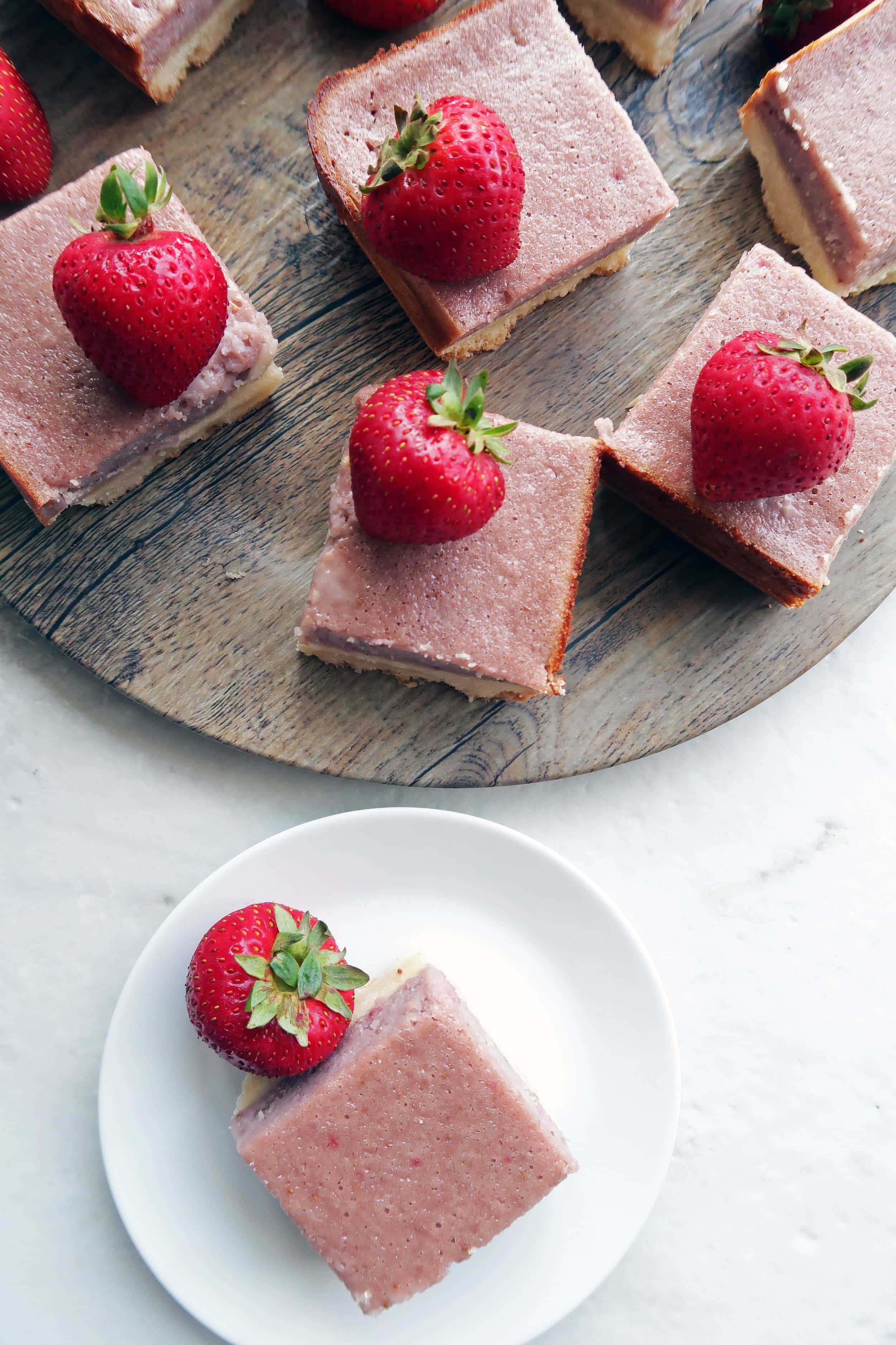 Pink strawberry shortbread bars on a round wooden platter and on a small white plate.