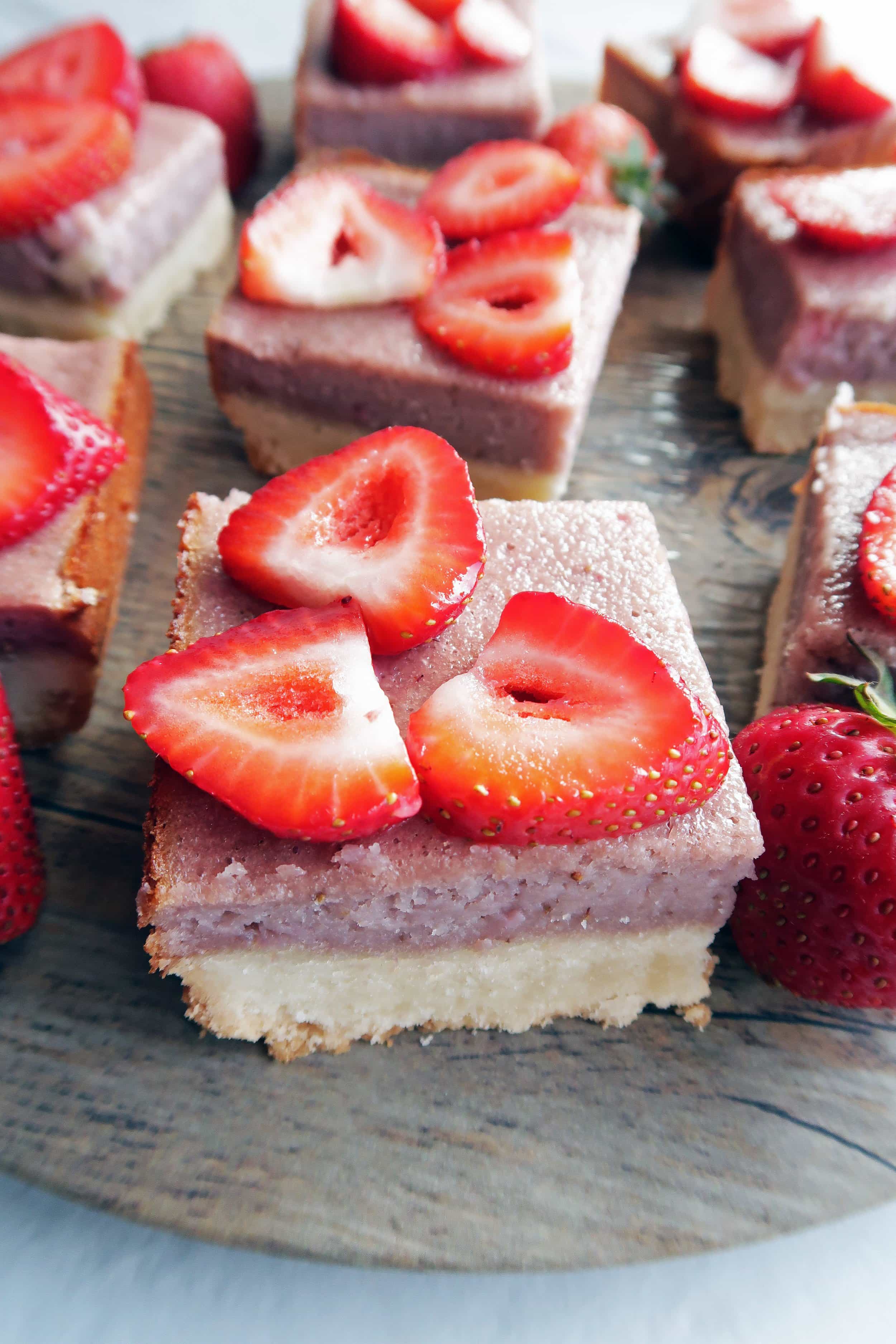 Closeup side angled view of a strawberry shortbread bar with strawberry slices on top -more in the background.