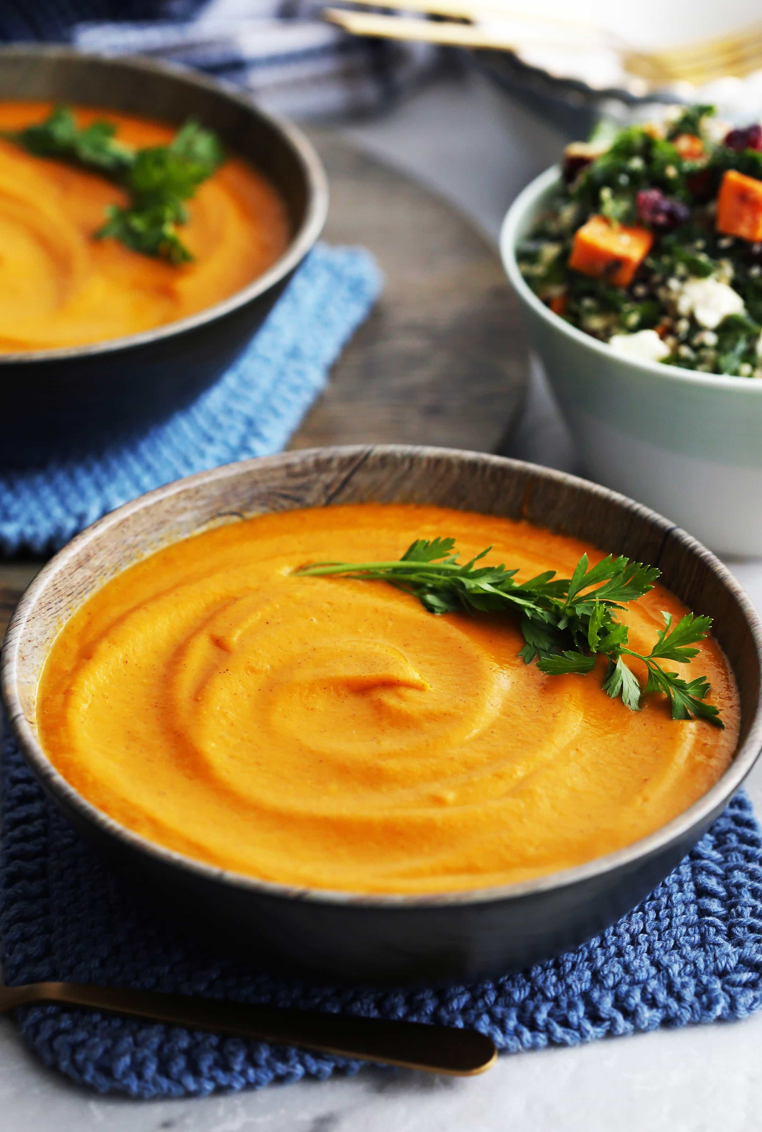 A wooden bowl of sweet potato carrot coconut soup made from the Instant Pot topped with parsley.