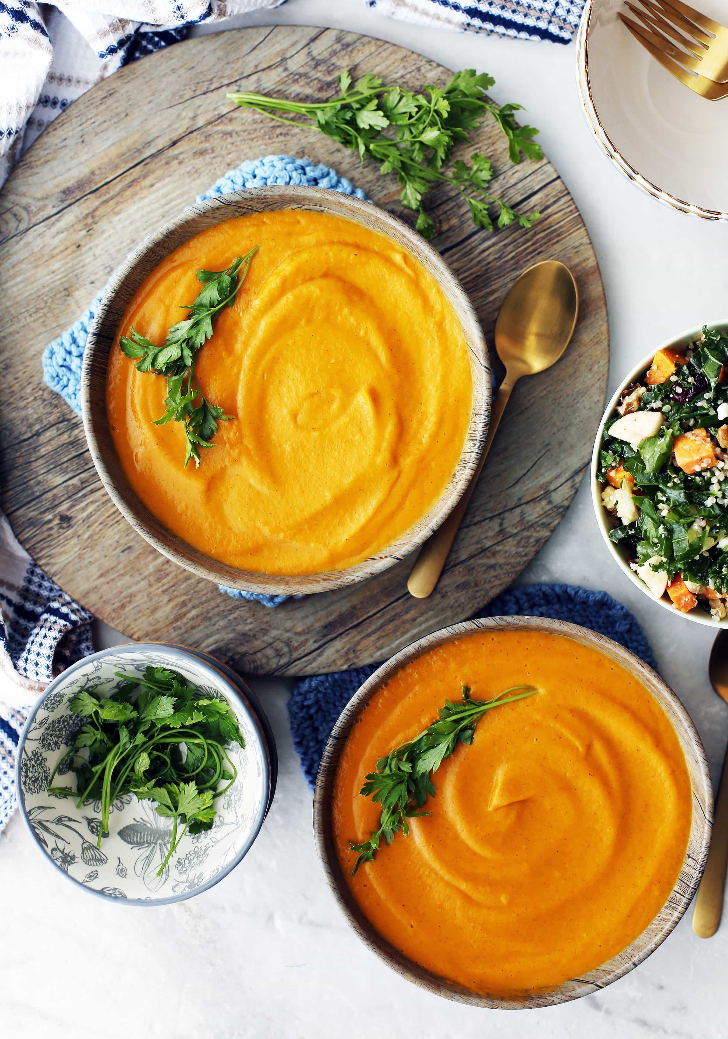 Two wooden bowls full of creamy orange Instant Pot sweet potato coconut soup with parsley garnish.