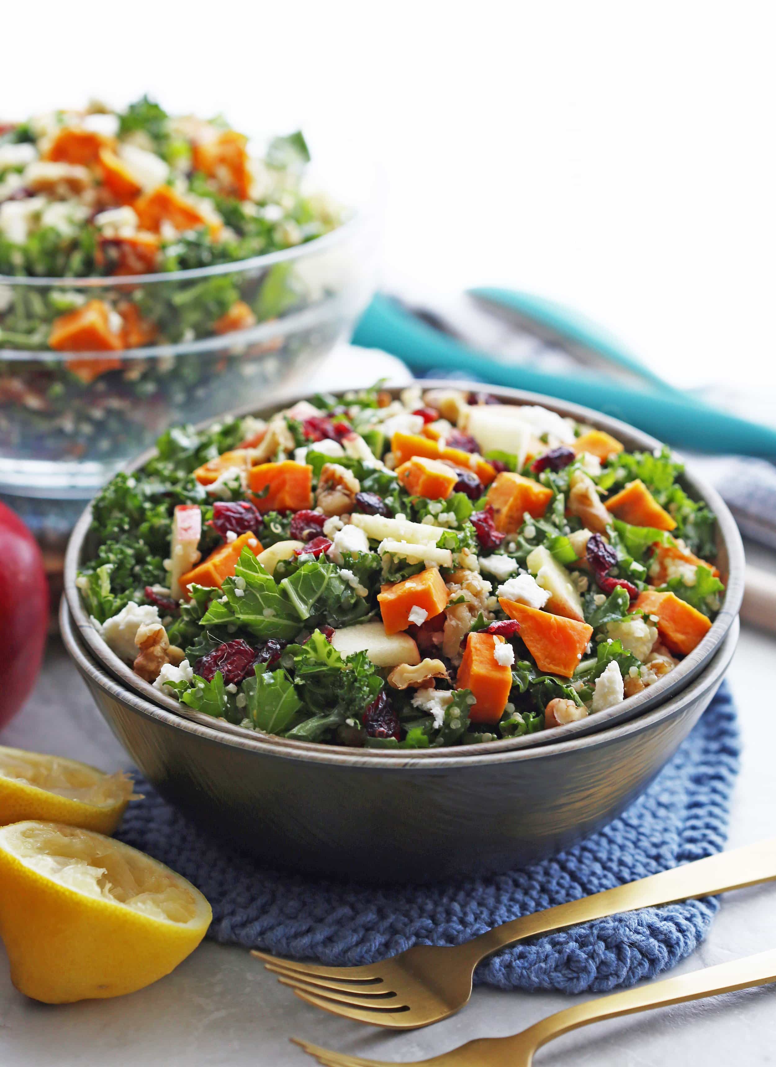 A bowl full of sweet potato salad with kale, walnuts, feta, quinoa, and dried cranberries.
