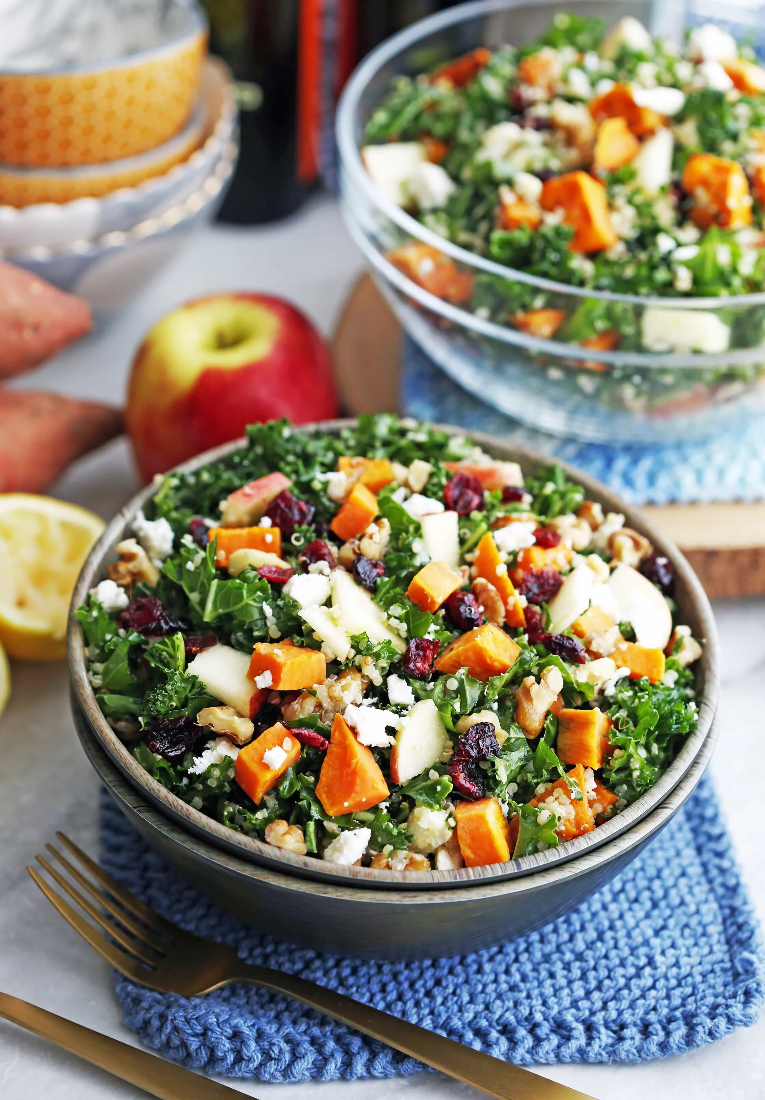 Sweet potato kale salad with feta, quinoa, dried cranberries, apple slices, and walnuts in a wooden bowl.
