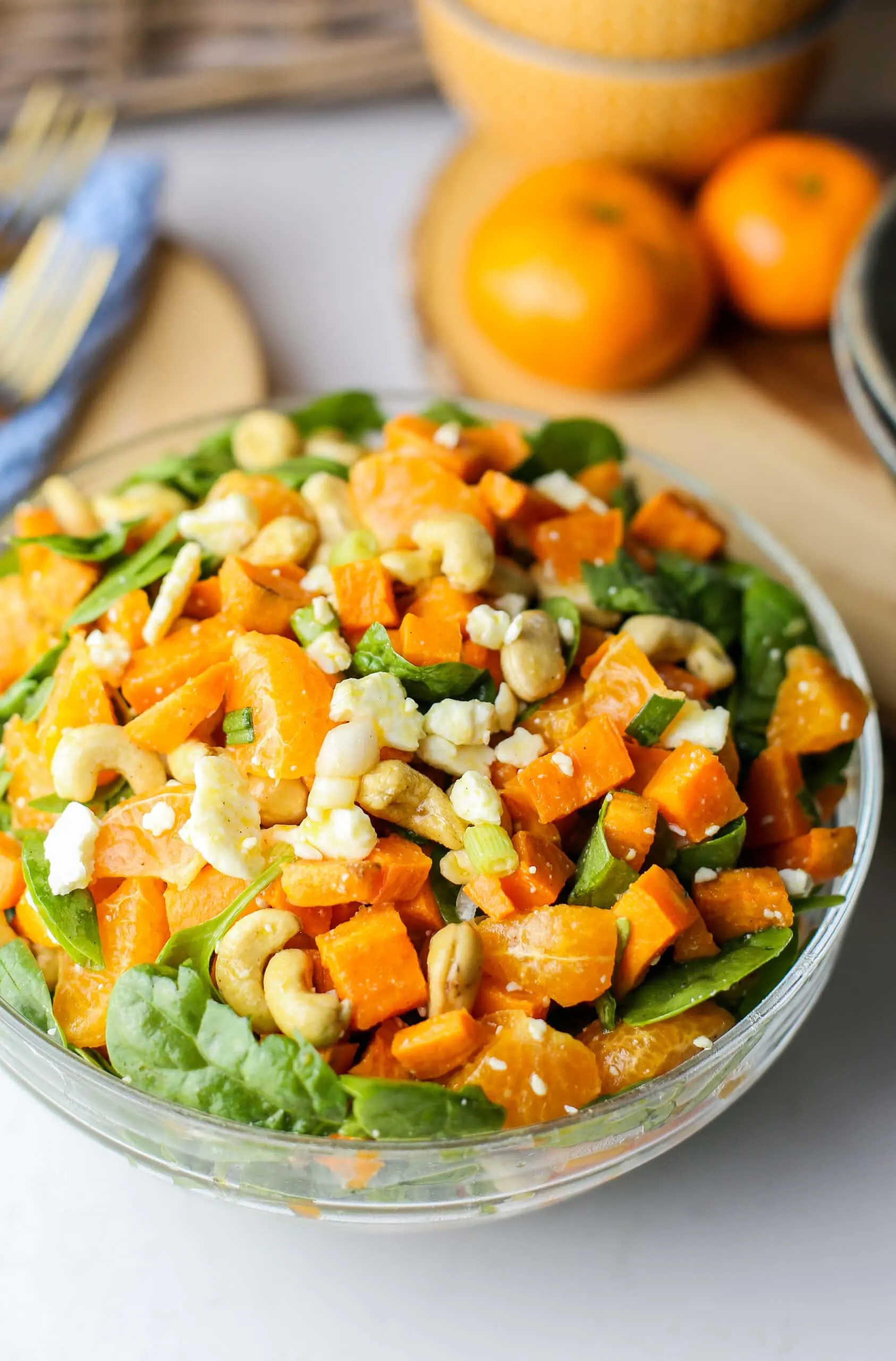 Sweet potato salad with feta, cashews, oranges, and spinach combined in a glass bowl.