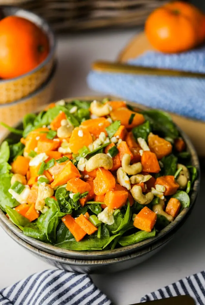 Top angled view of a wooden bowl containing sweet potato orange spinach salad.