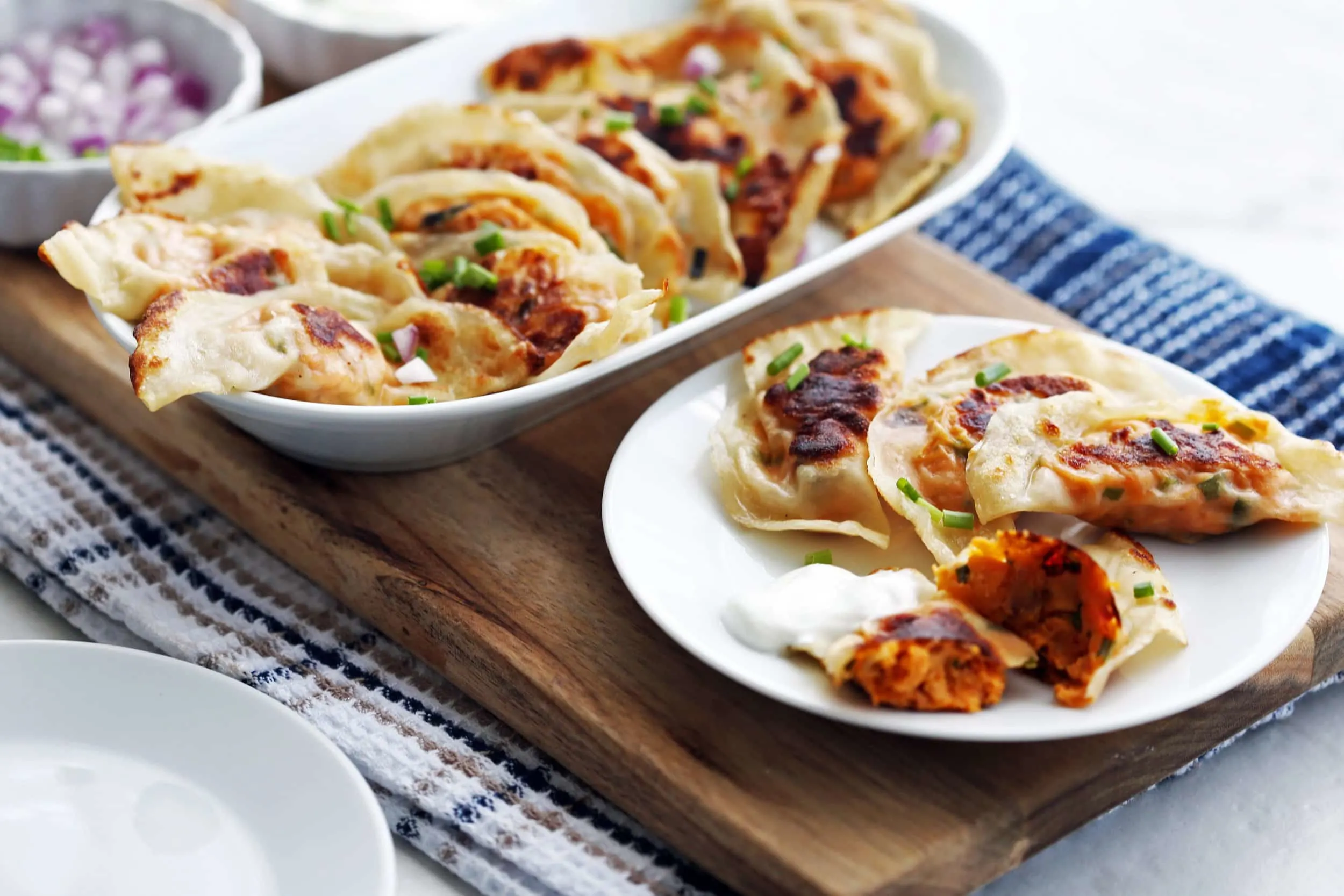 A long platter and plate full of crispy sweet potato cream cheese potstickers.