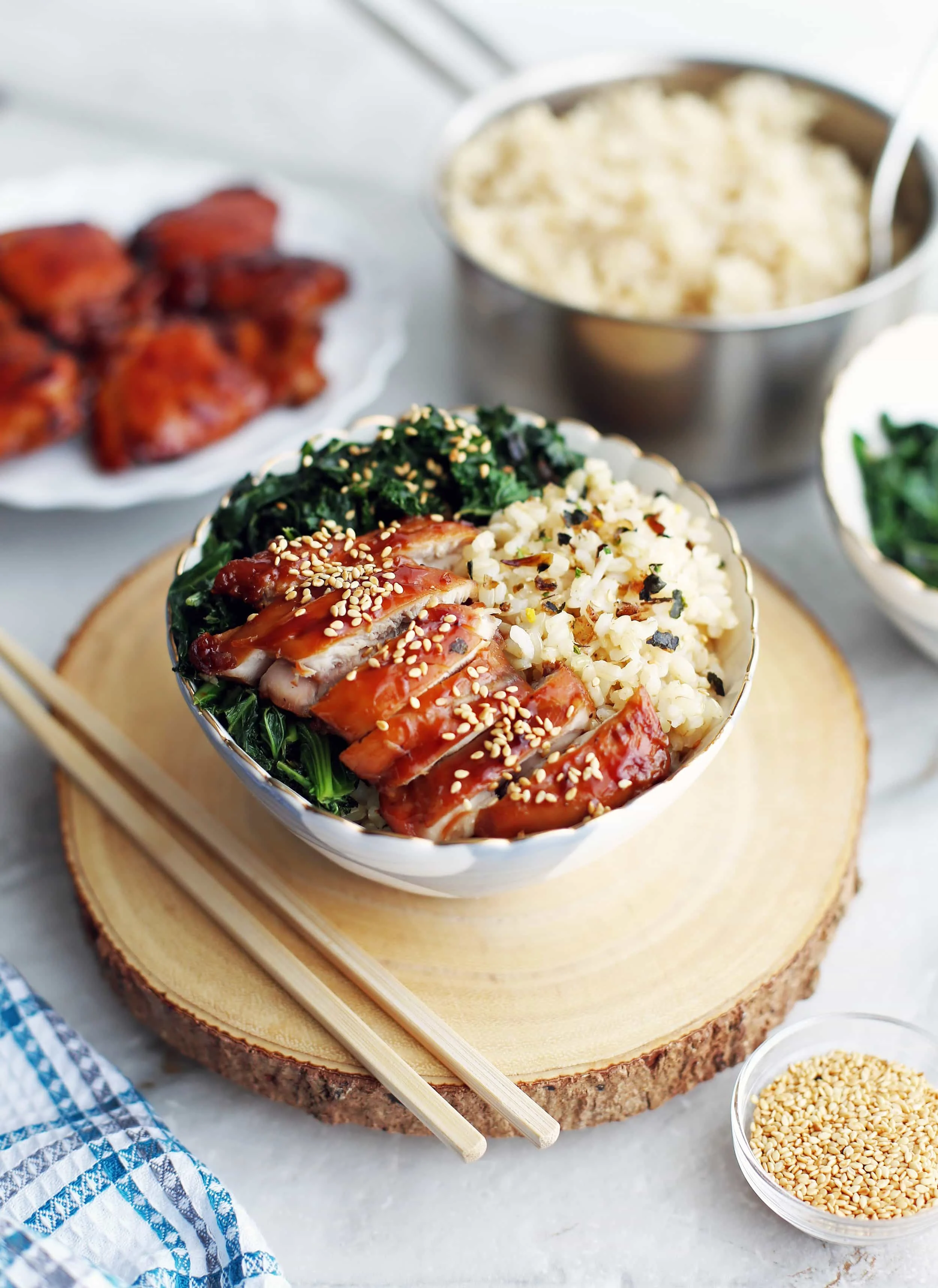 Side view of a bowl of teriyaki chicken with green sauteed kale, and brown rice.