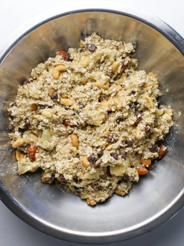 Trail mix, mashed bananas, and oats combined in a stainless steel bowl.