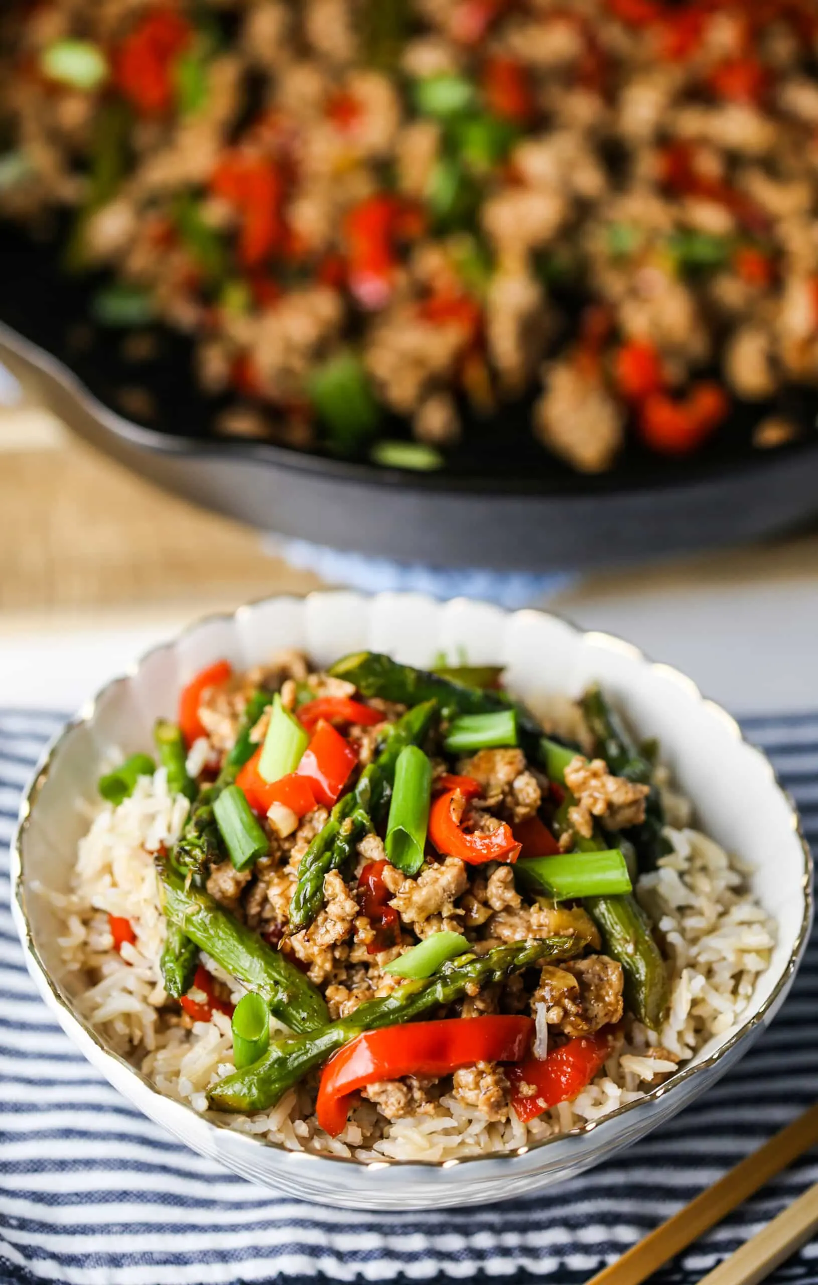 A top angle view of turkey asparagus stir-fry in a blue and white bowl and in a cast iron skillet.
