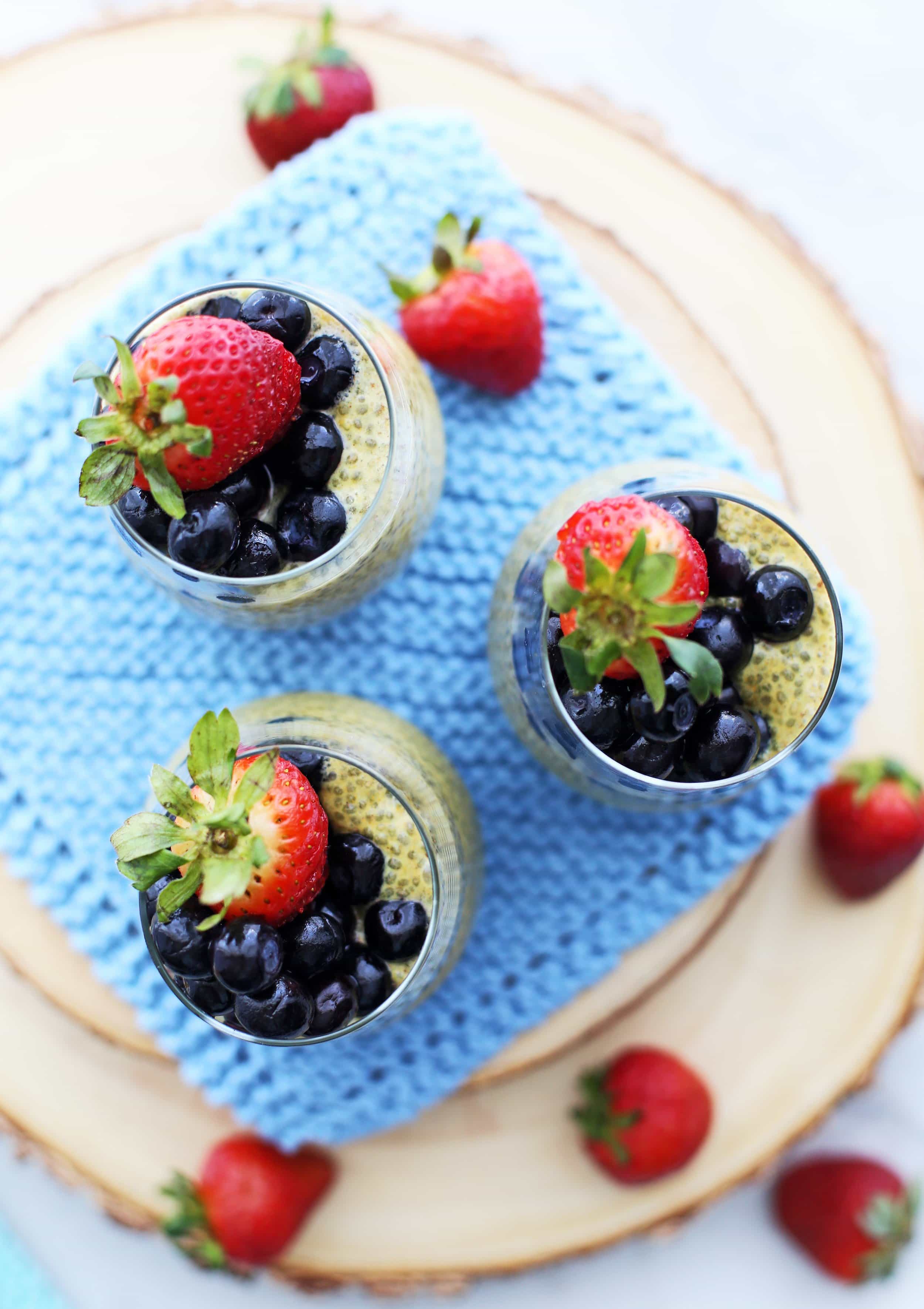 Overhead view of three glasses of turmeric milk chia pudding with strawberries and blueberries.