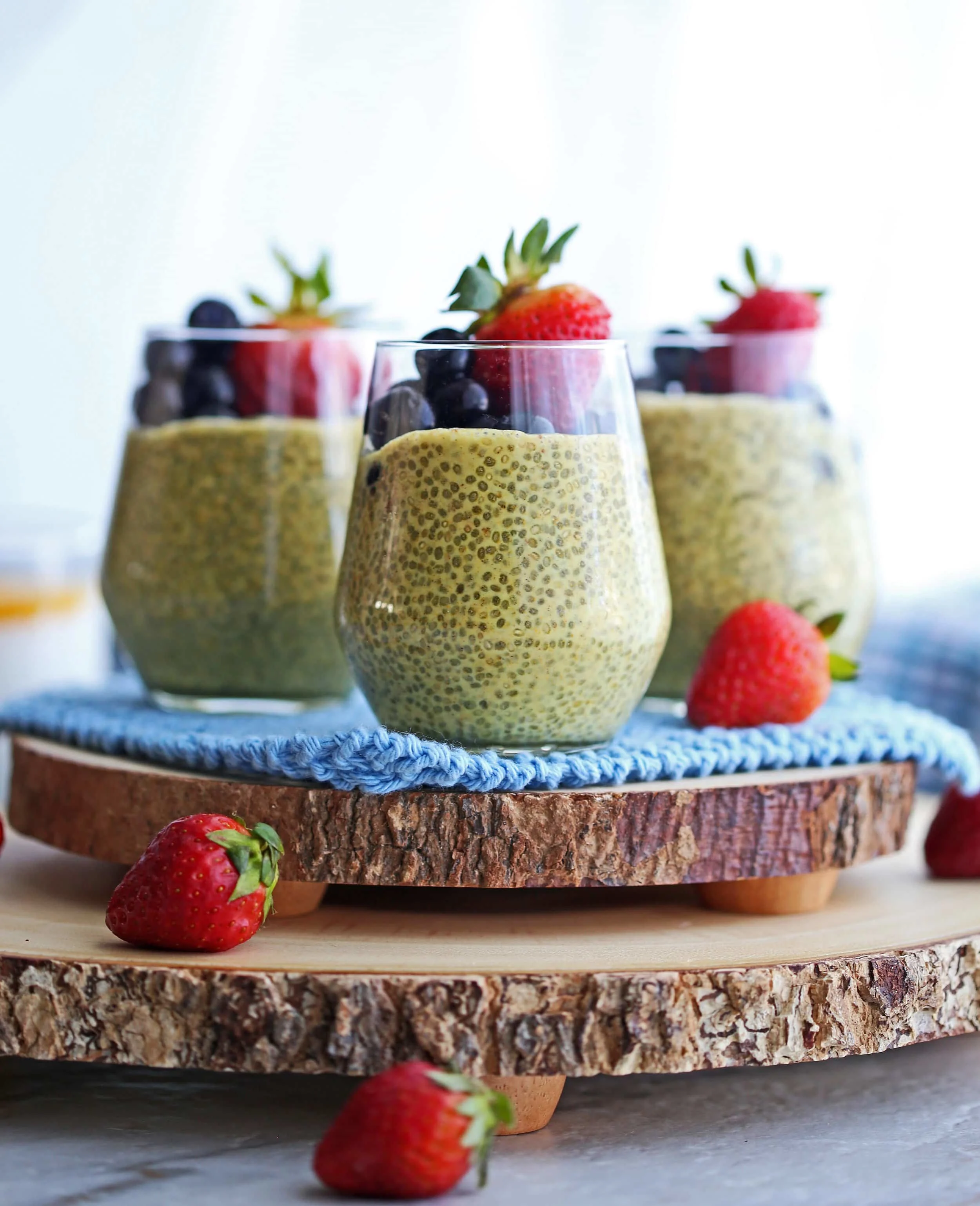 Side view of three glasses full of turmeric milk chia pudding with strawberries and blueberries on a wooden slab.
