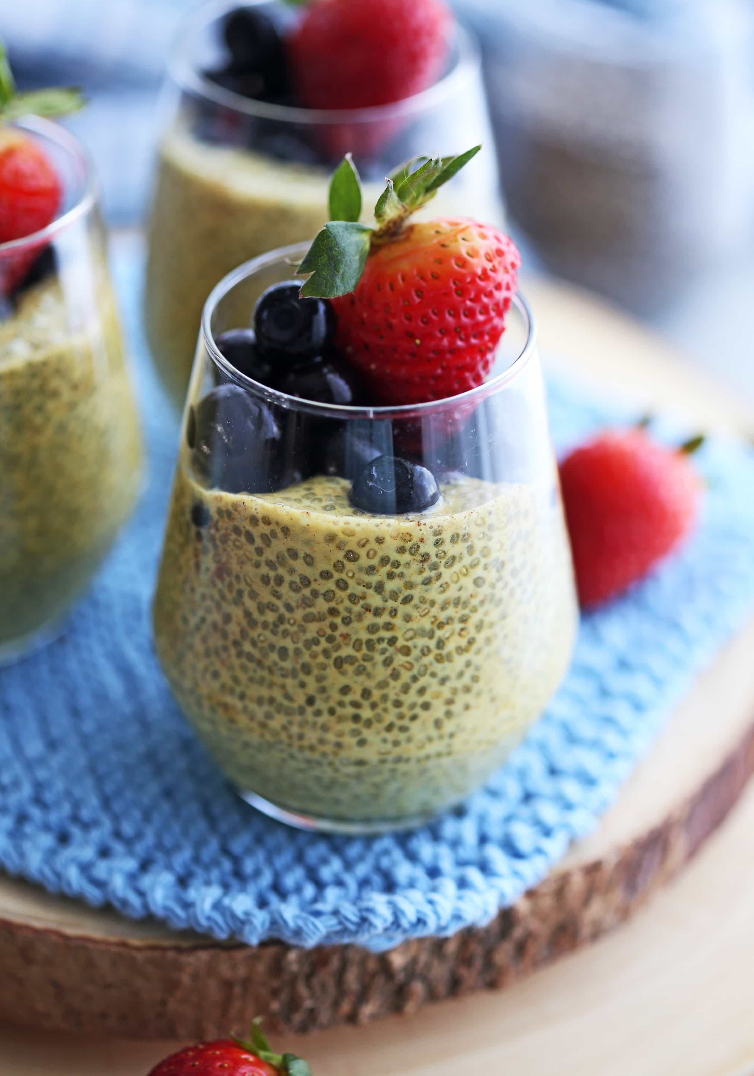 Close up view of a glass of turmeric milk chia pudding with blueberries and strawberries.