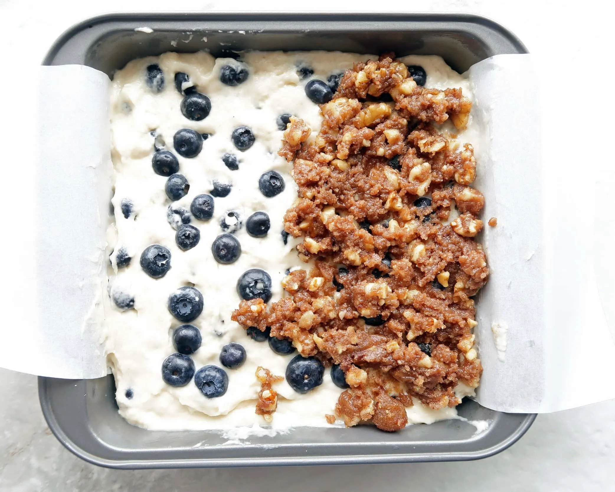 Blueberry coffee cake batter with a brown sugar-walnut crumble in a square baking pan.