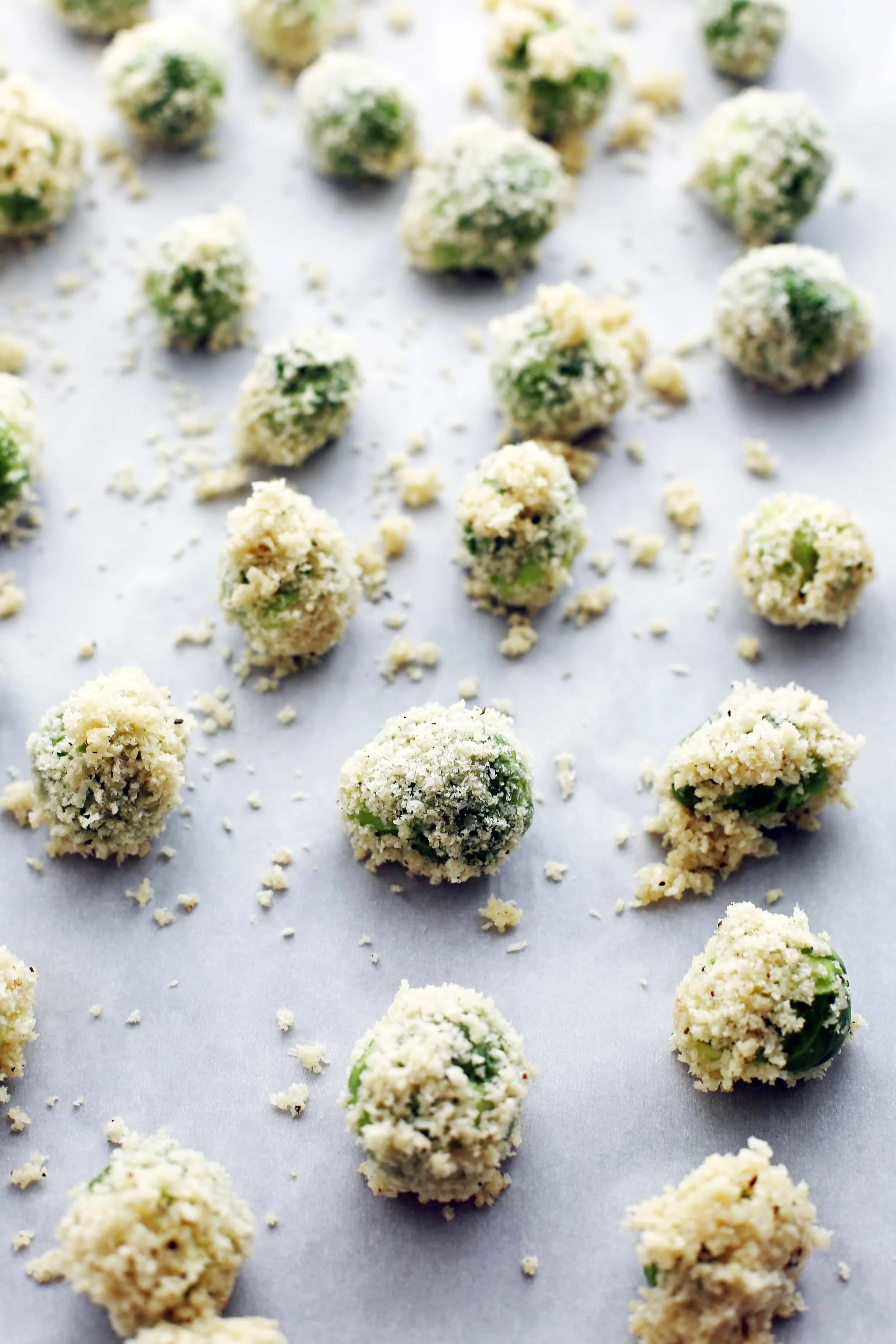 Brussels sprouts coated in a parmesan breadcrumb dredge on a parchment paper lined baking sheet.