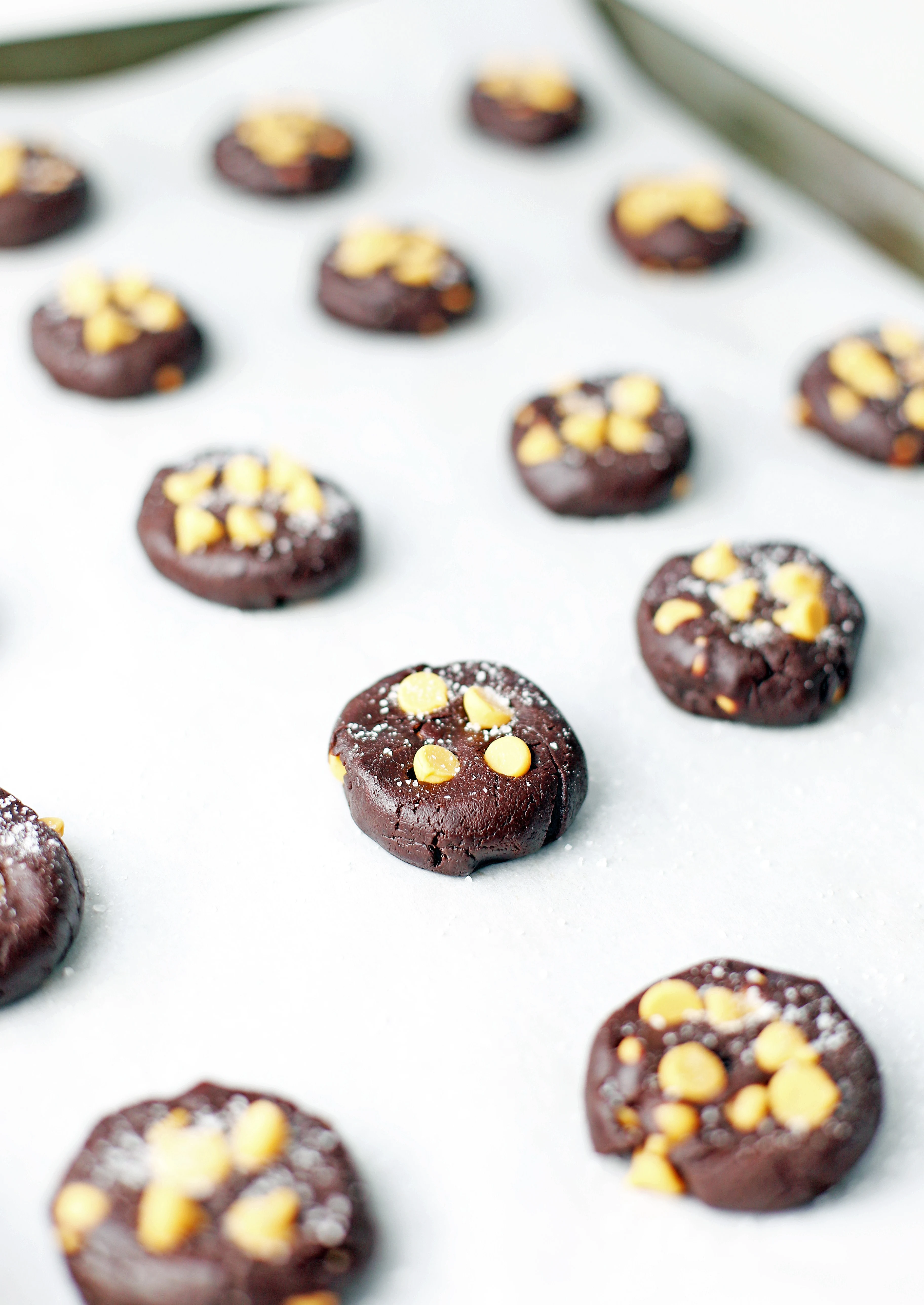 Side view of unbaked salted chocolate butterscotch chip cookies on a parchment paper lined baking sheet.