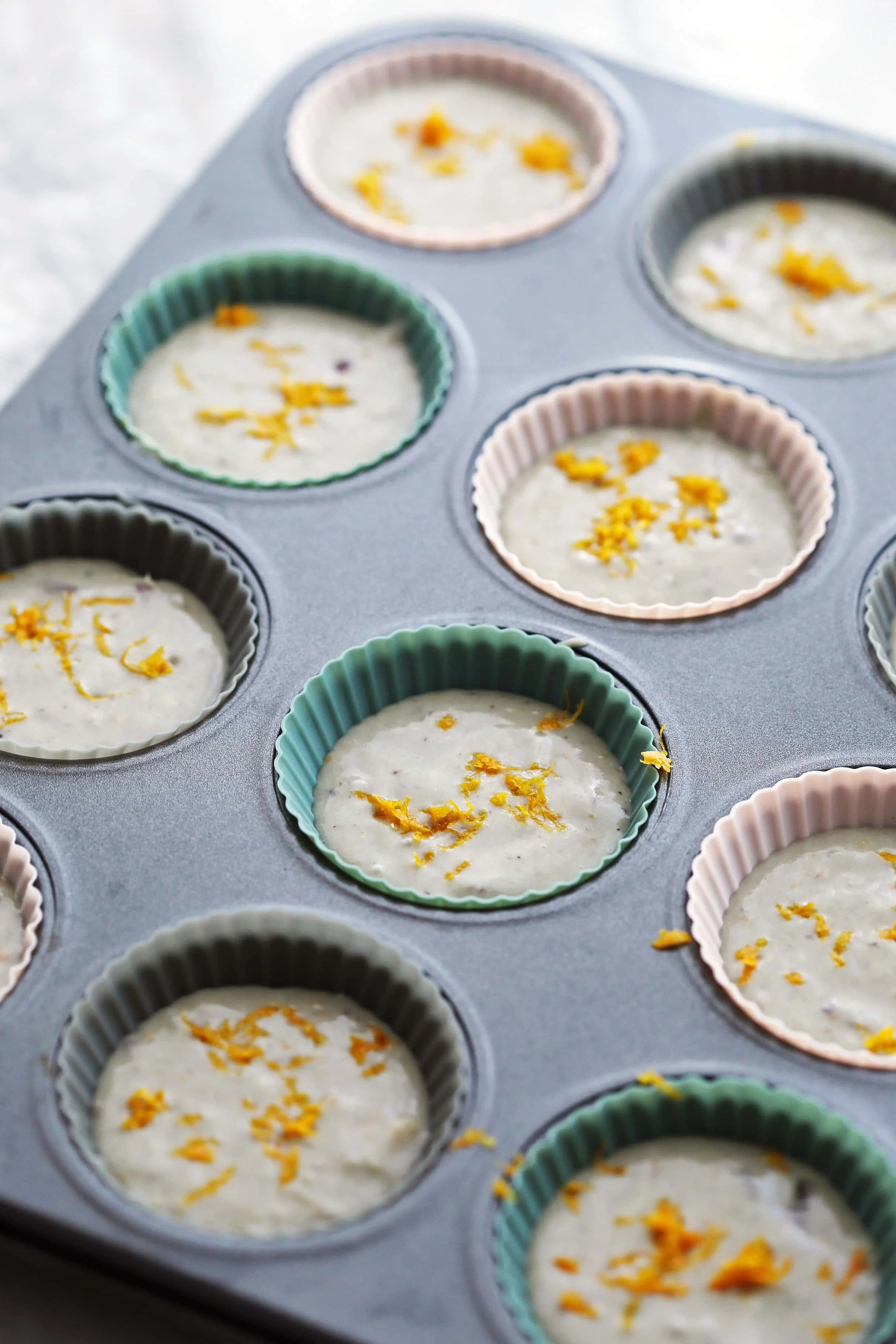 Cranberry orange muffin batter poured into a muffin pan with orange zest on top.