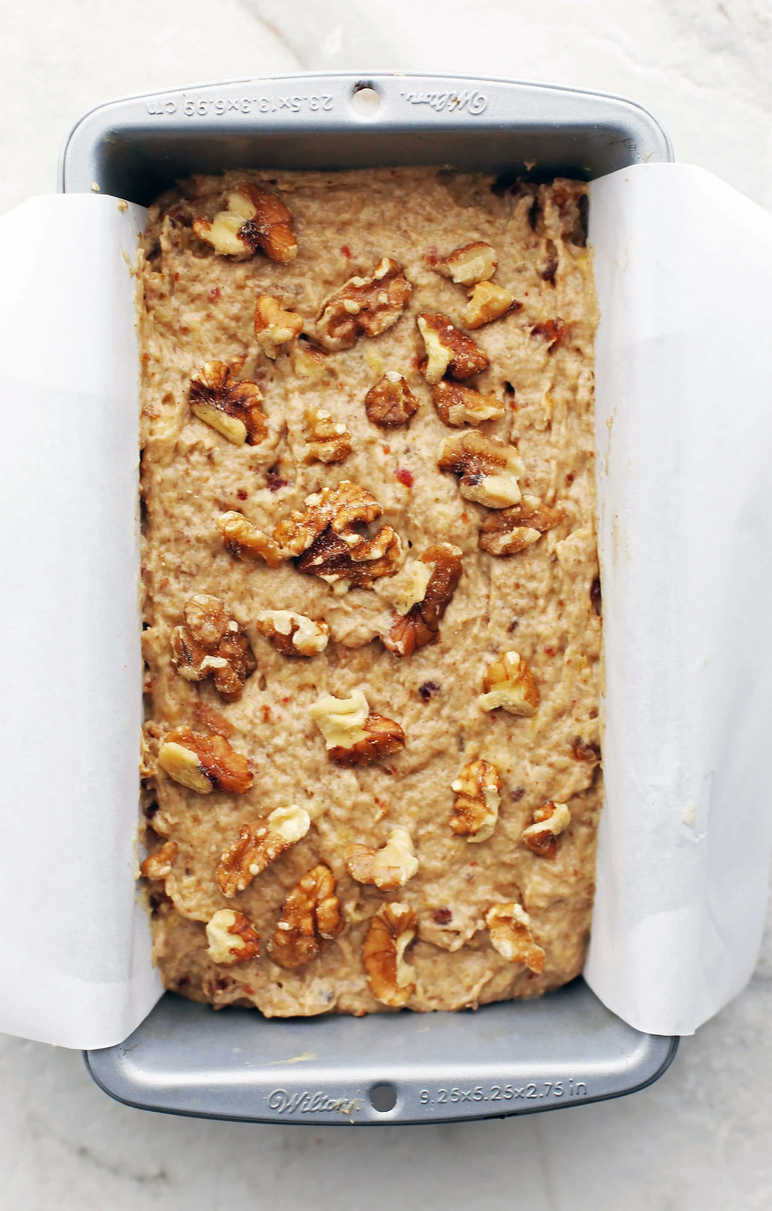Date Banana Nut Bread dough topped with walnuts in a parchment paper-lined loaf pan.