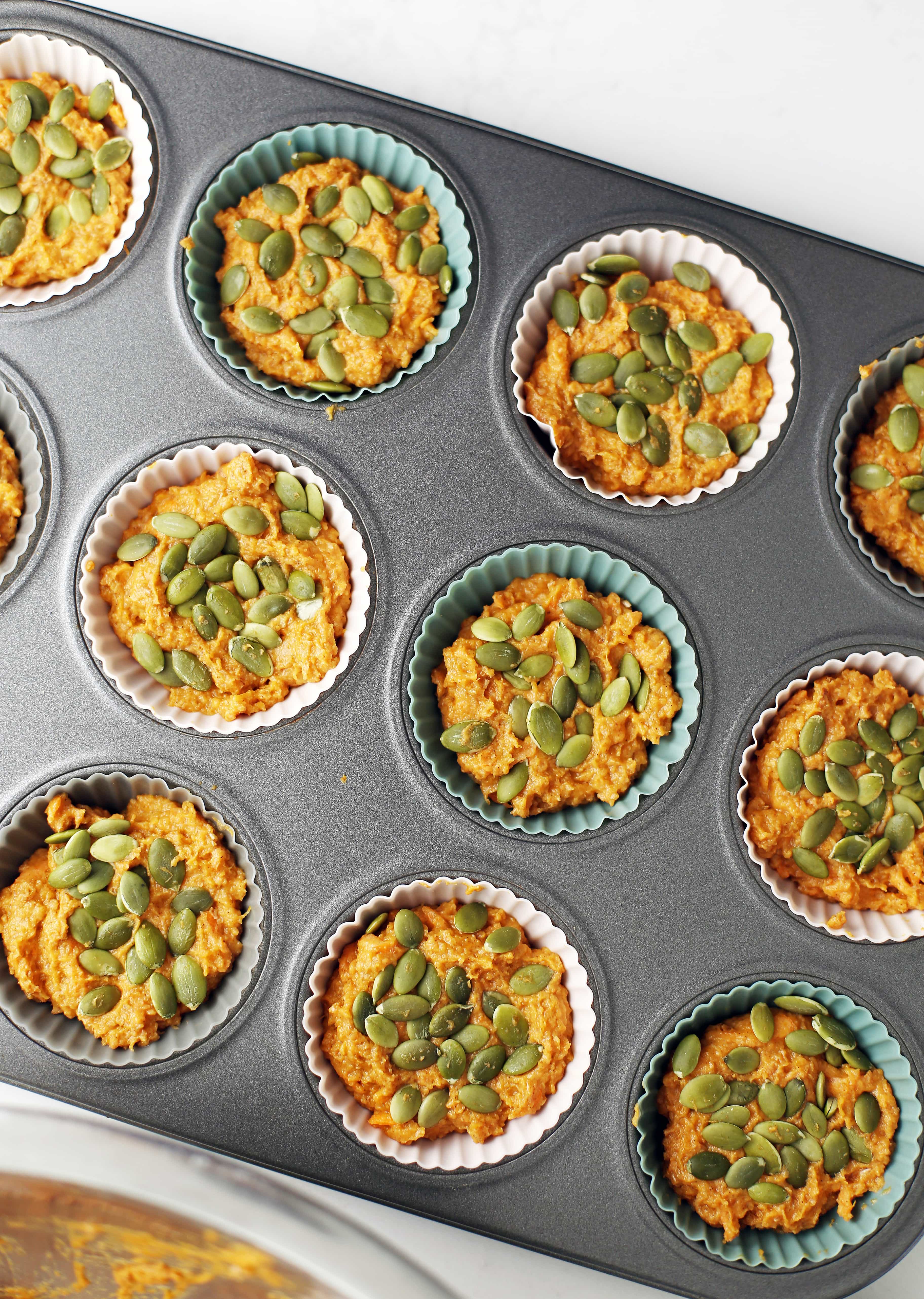Overhead view of carrot pumpkin muffin batter scooped in a muffin pan and topped with pumpkin seeds. 