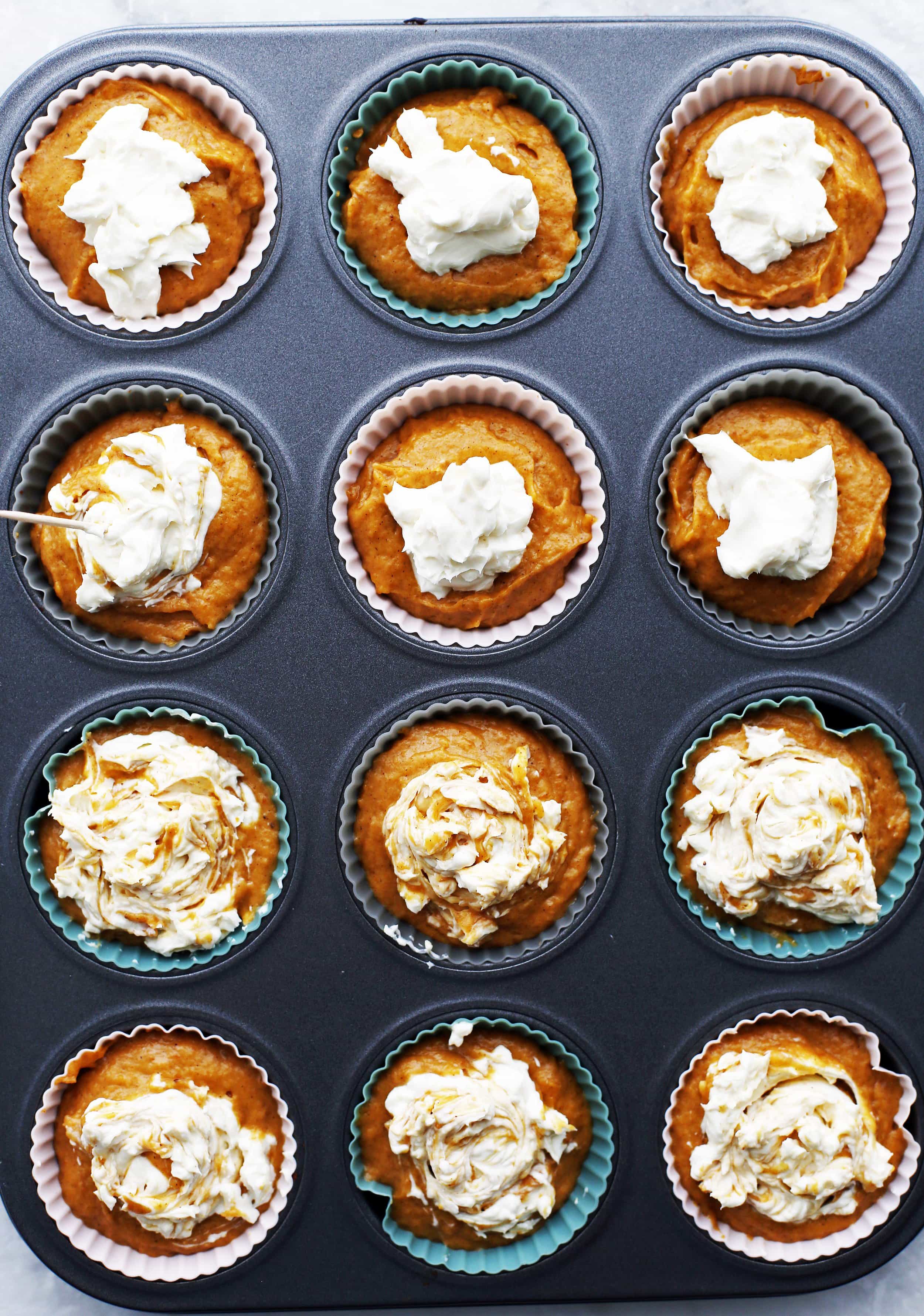 Twelve unbaked pumpkin cream cheese muffins in a muffin pan.