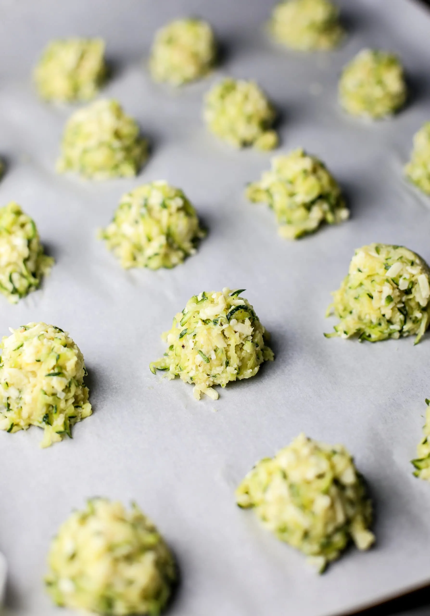 Unbaked zucchini bites on top of a parchment paper lined baking sheet.