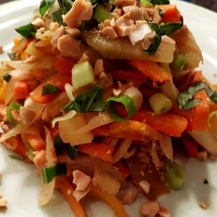 Vegetable Pad Thai on a white plate topped with Thai basil and peanuts.