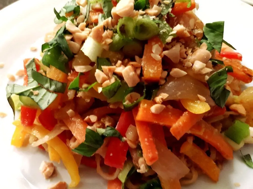 Overhead close-up of Vegetable Pad Thai topped with Thai basil and peanuts.