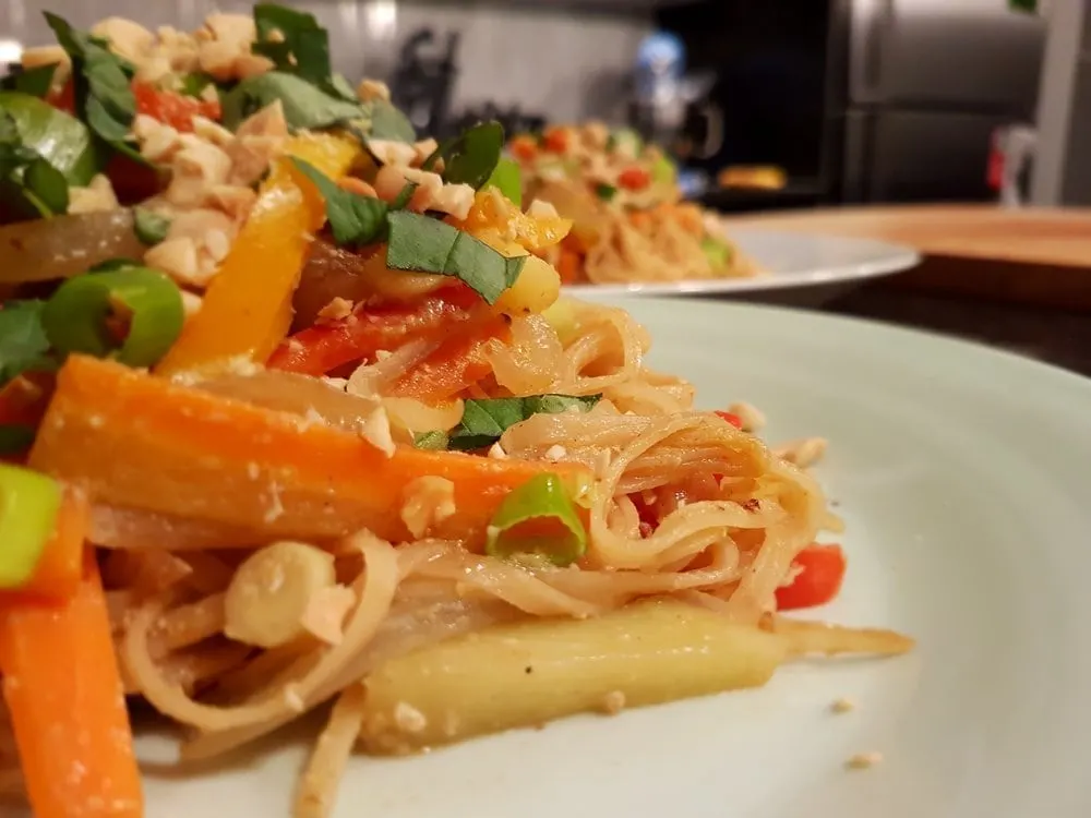A plate of noodles, crisp fresh vegetables, Thai basil, and peanuts.