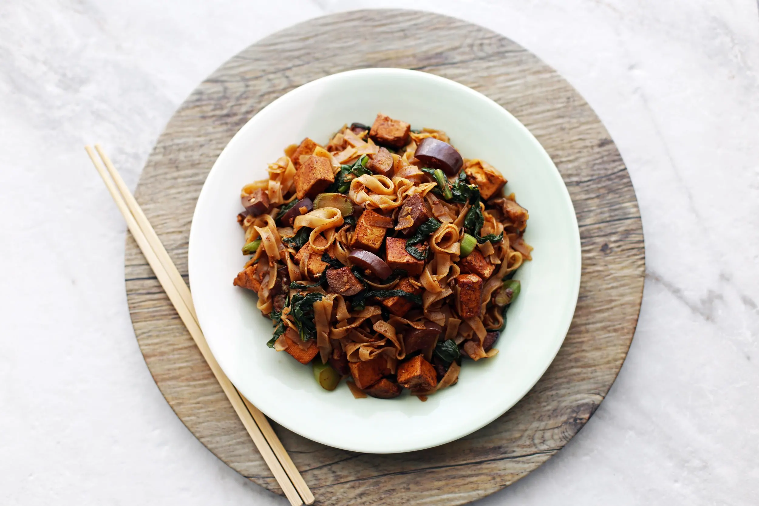 a plate of Vegetarian Pad See Ew topped with Thai basil, ready to eat