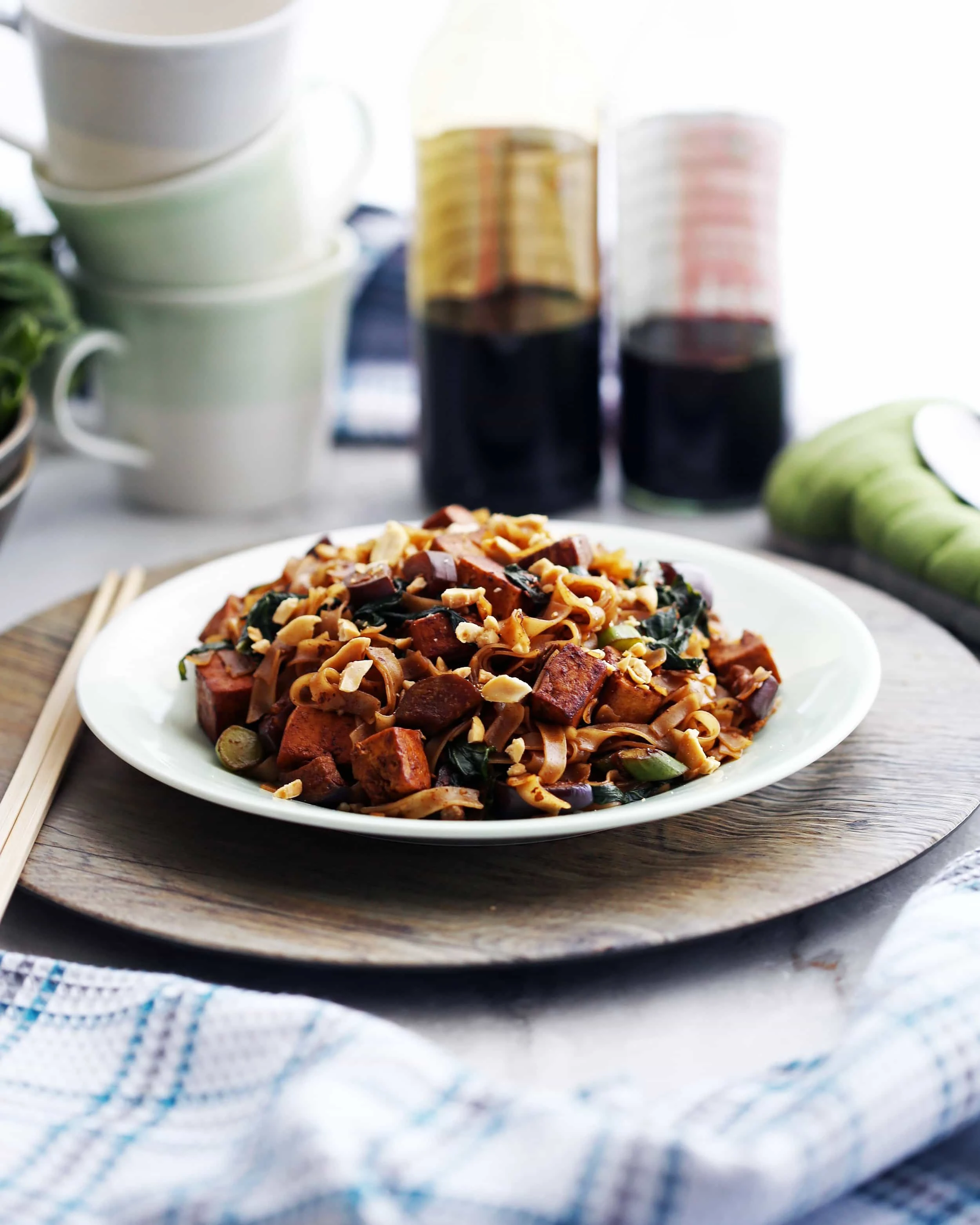 Side view of vegetarian pad see ew with tofu and Chinese eggplant on a white plate.