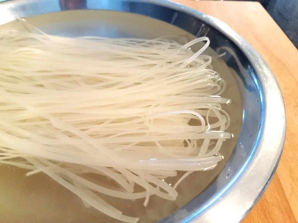 Rice noodles soaking in a metal bowl.