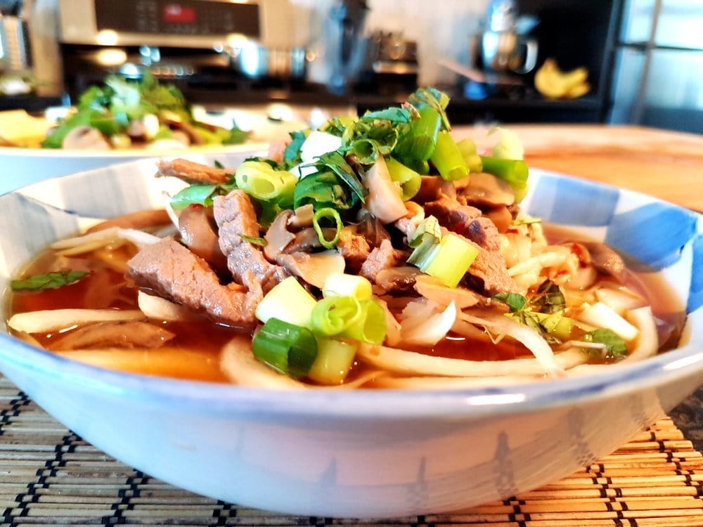 A bowl of noodles in beef broth topped with green onions.