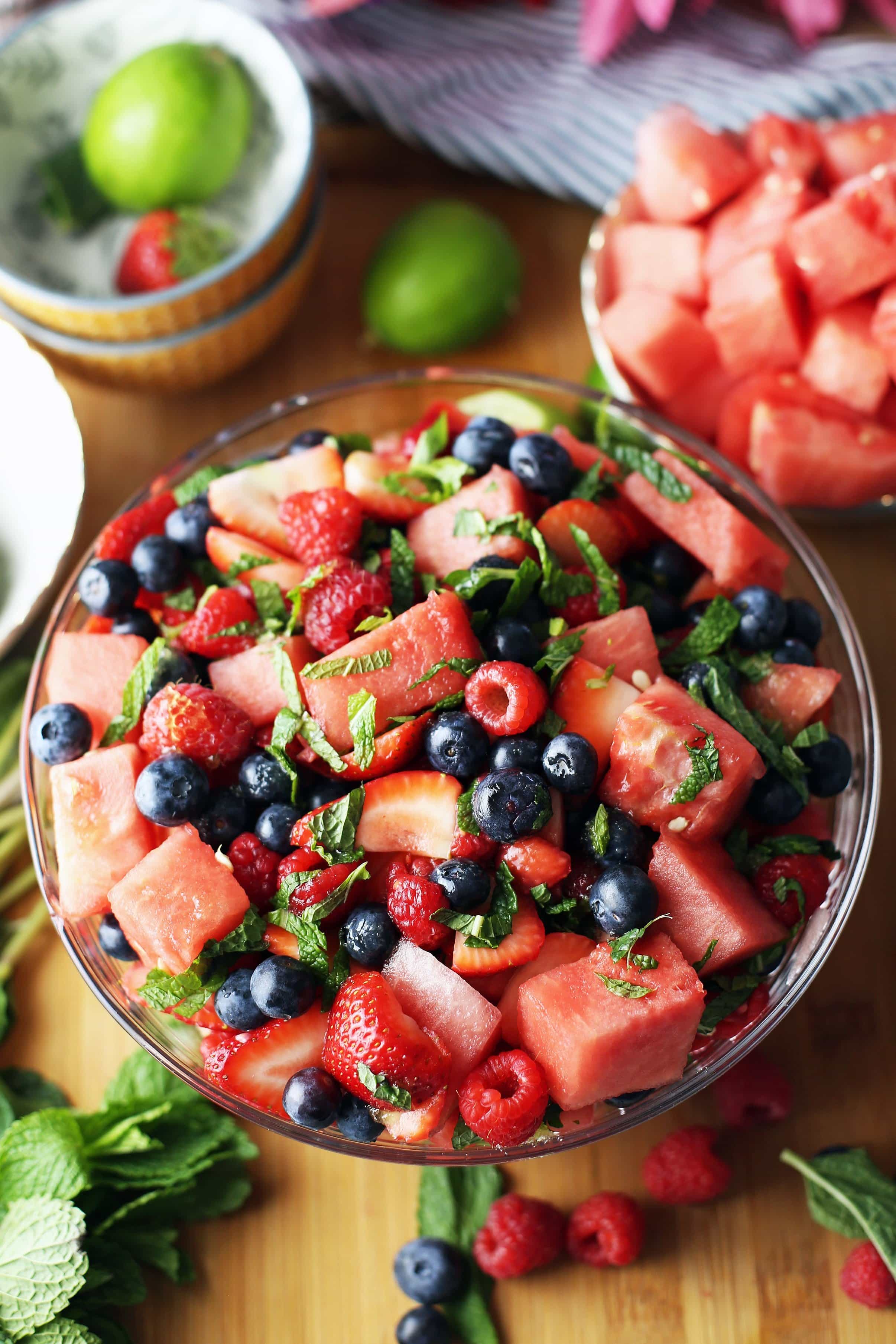 A glass bowl containing a watermelon and berry salad topped with sliced fresh mint.