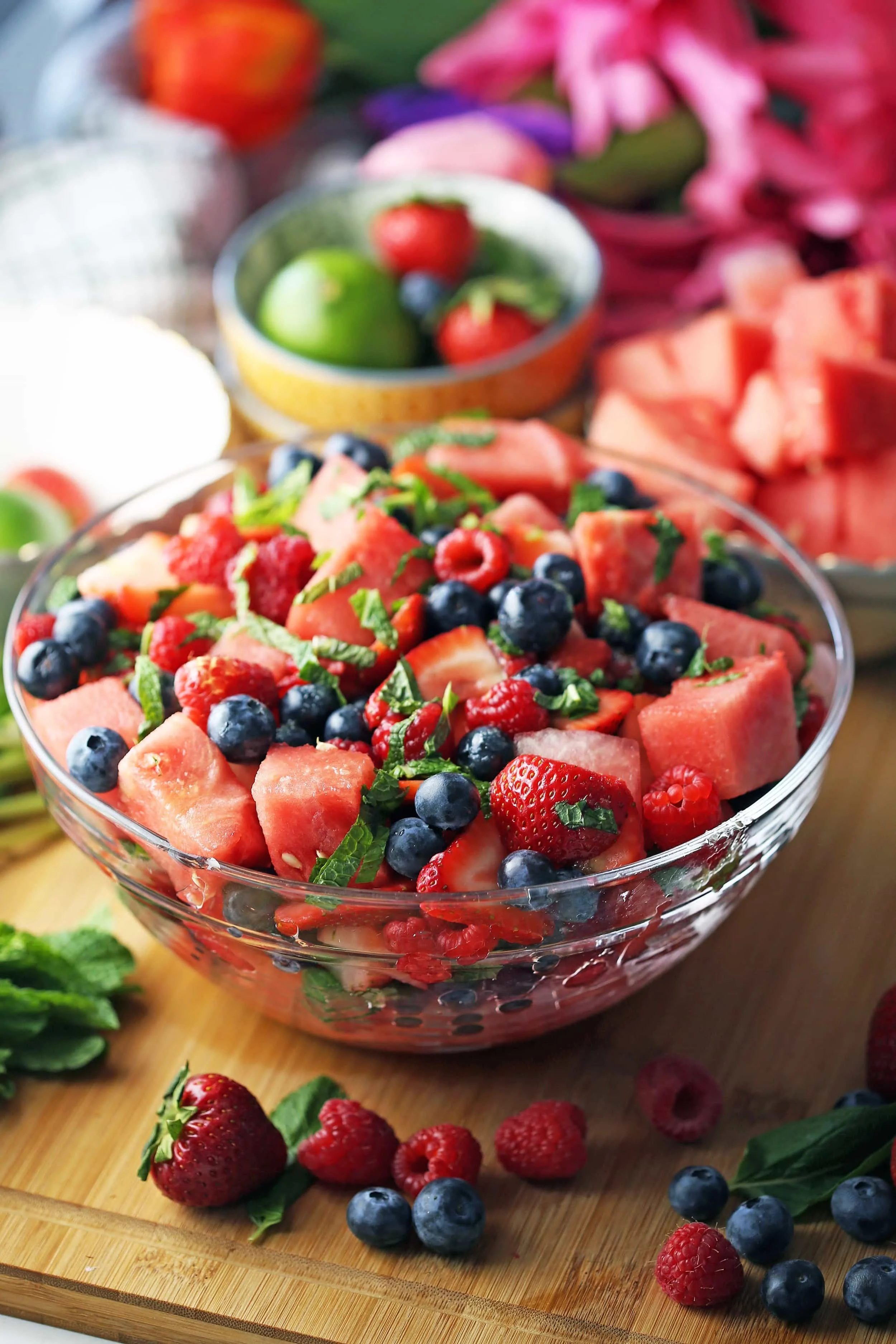 Watermelon berry summer salad in a glass bowl surrounded by more berries, watermelon pieces, and fresh mint.