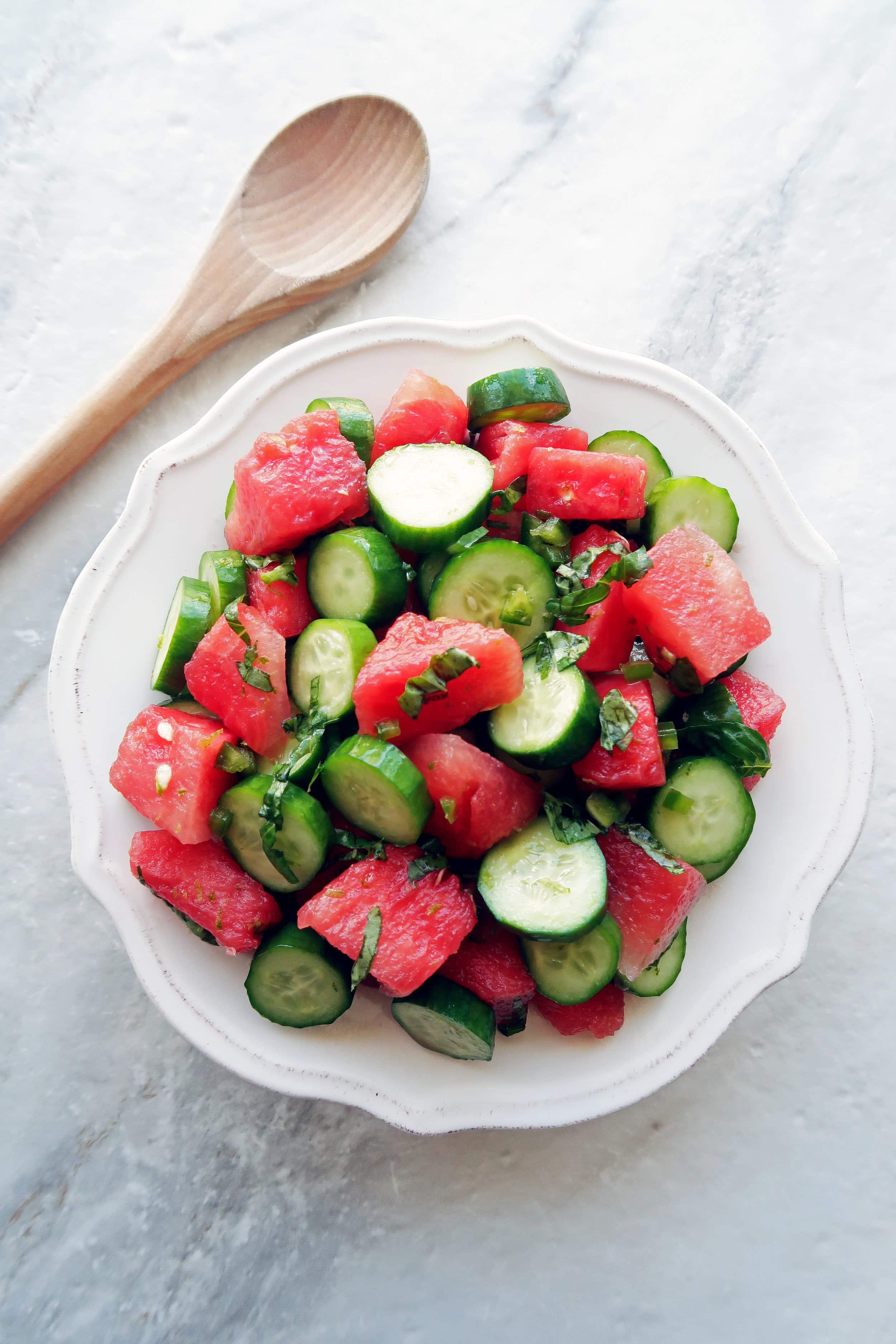 Watermelon Cucumber Jalapeno Salad on a white plate with a wooden spoon on the side of the plate.