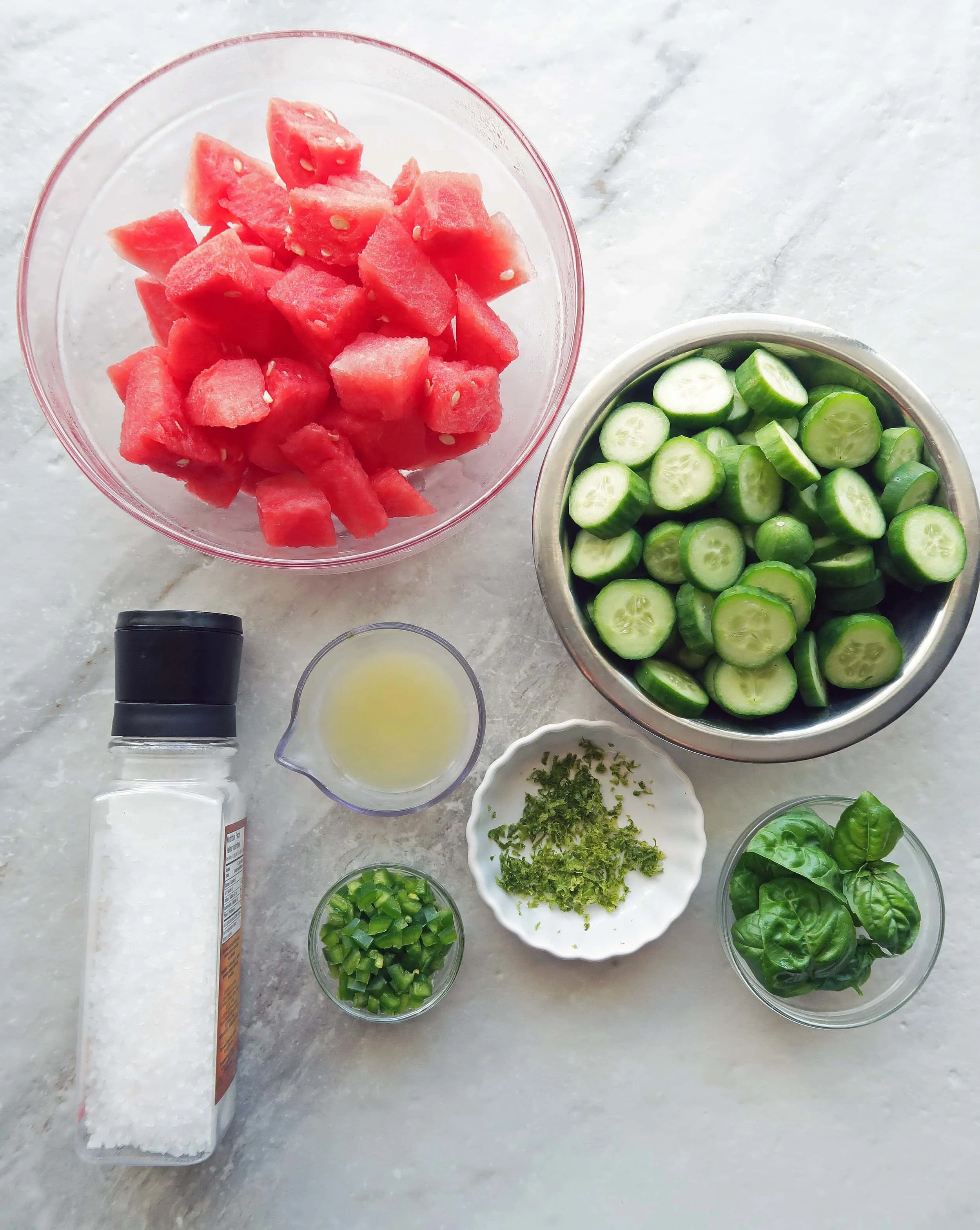 Bowls containing chopped watermelon, cucumber, and jalapeno along with lime zest, lime juice, and basil leaves.