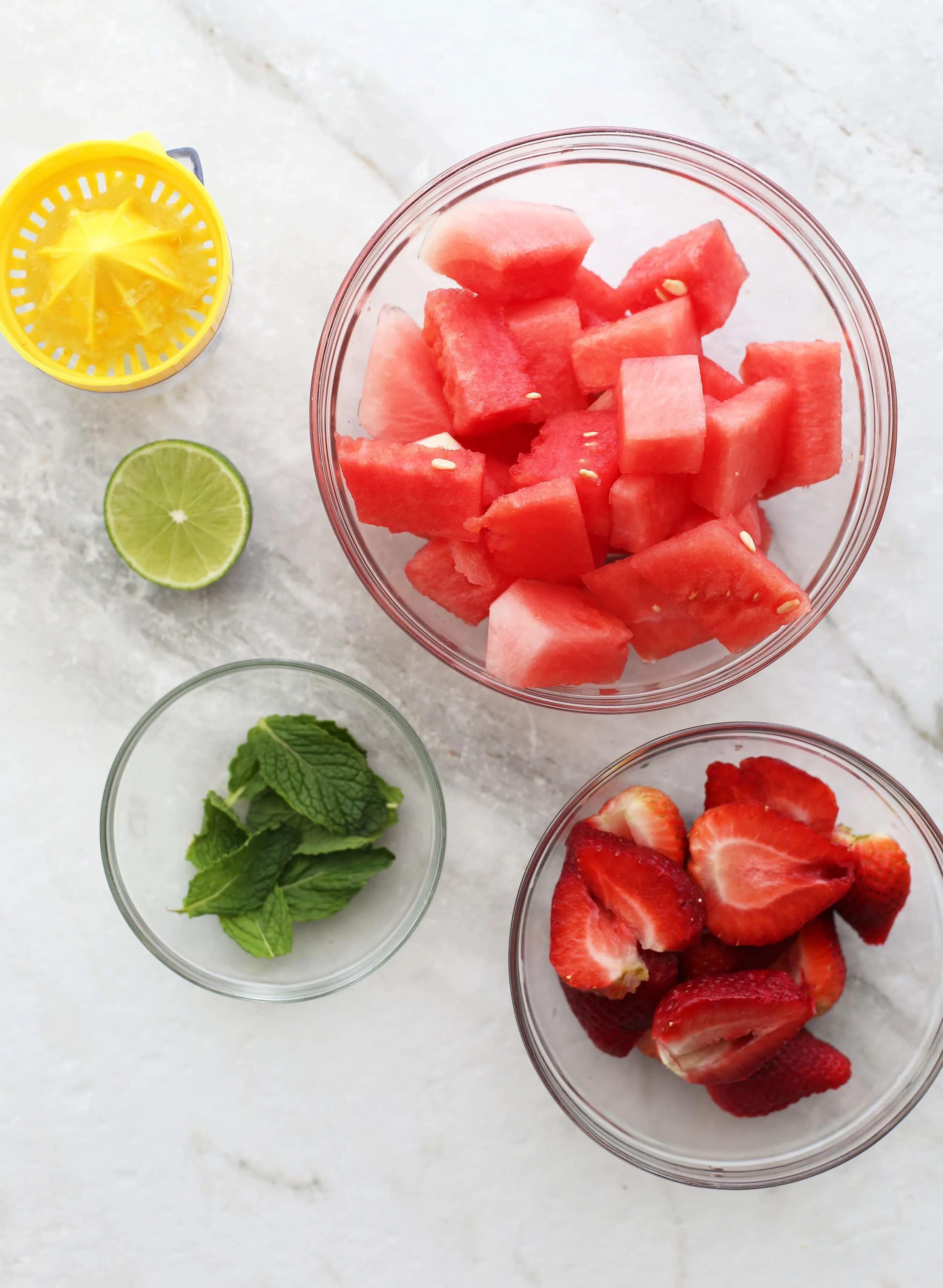 Bowls of strawberries, watermelon, fresh mint, and half a lime.