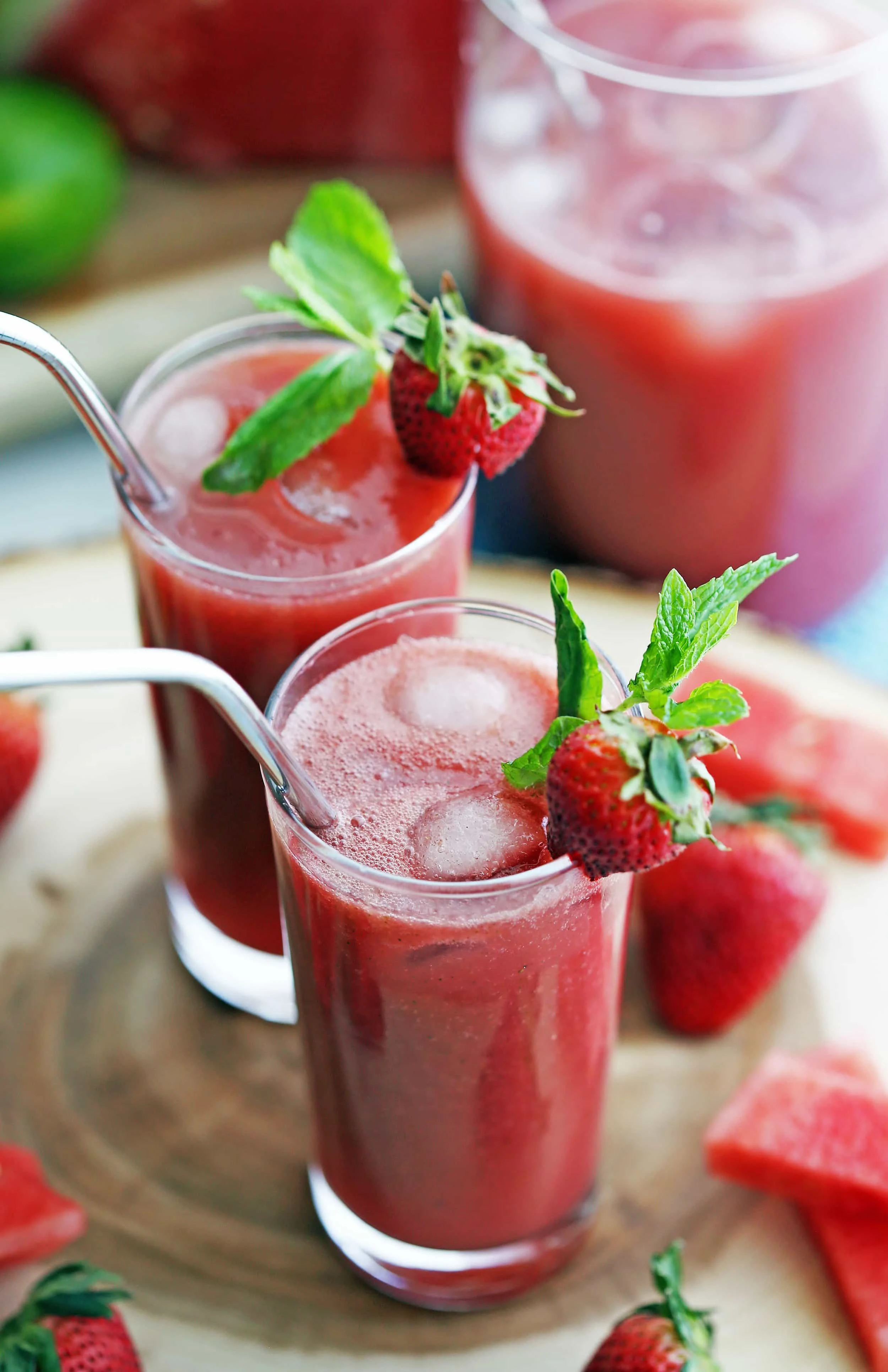 Two glasses of Fresh Watermelon Strawberry Soda with ice and strawberry and mint garnish on a wooden platter.