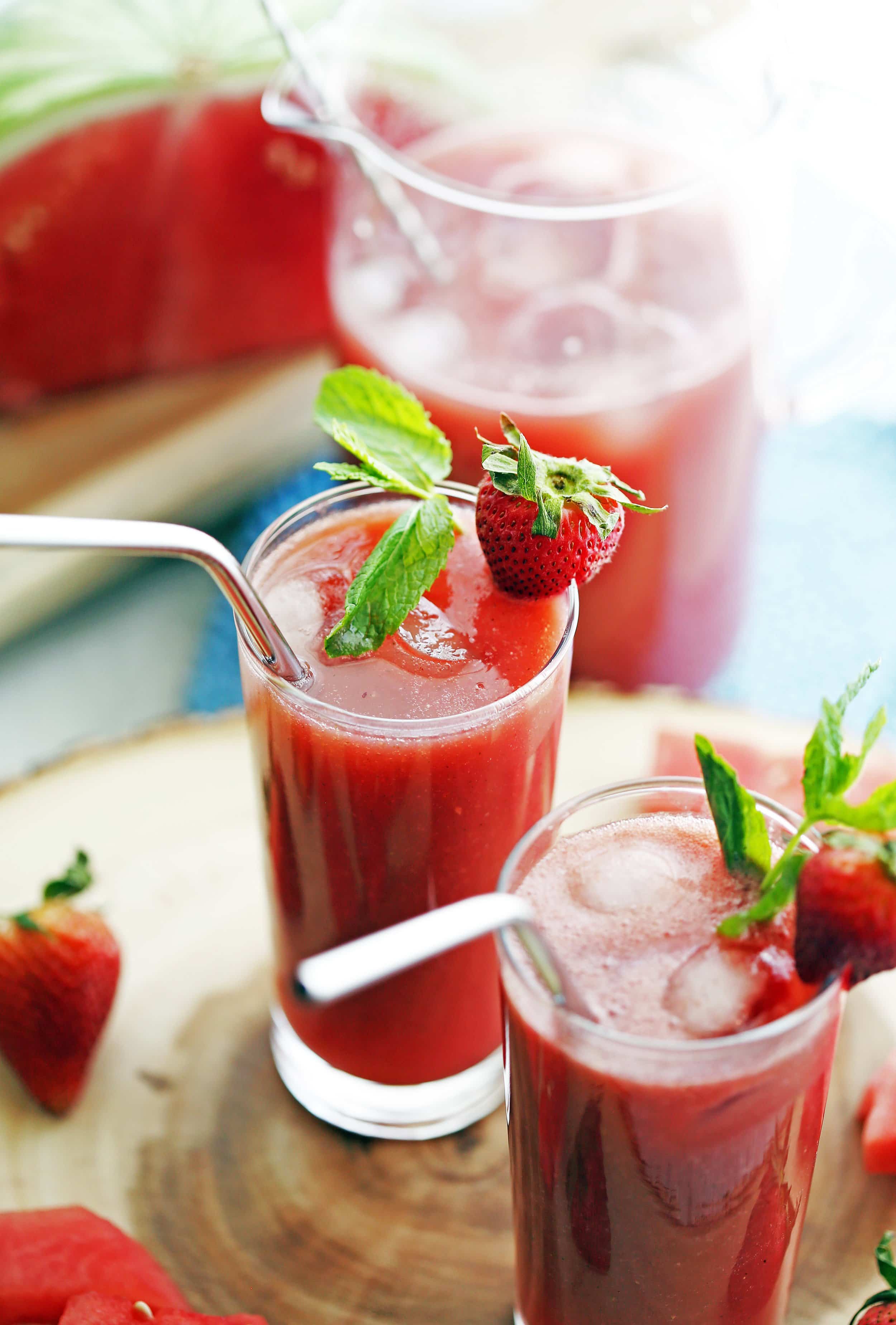 Two tall glasses full of Fresh Watermelon Strawberry Soda with ice and strawberry and mint garnish.