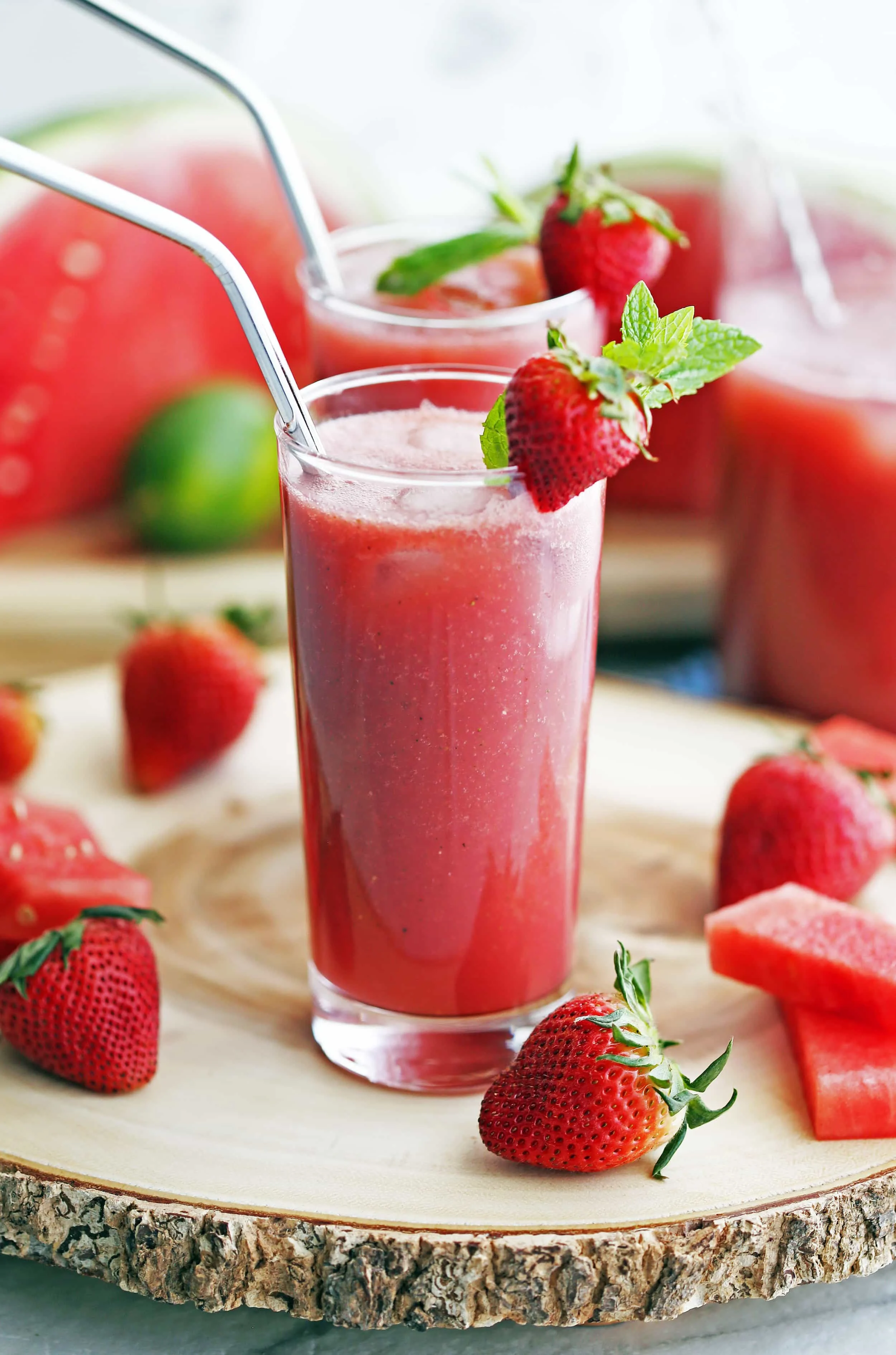 Fizzy Fresh Watermelon Strawberry Sodas garnished with strawberries and mint in two tall glasses on a round wooden platter.