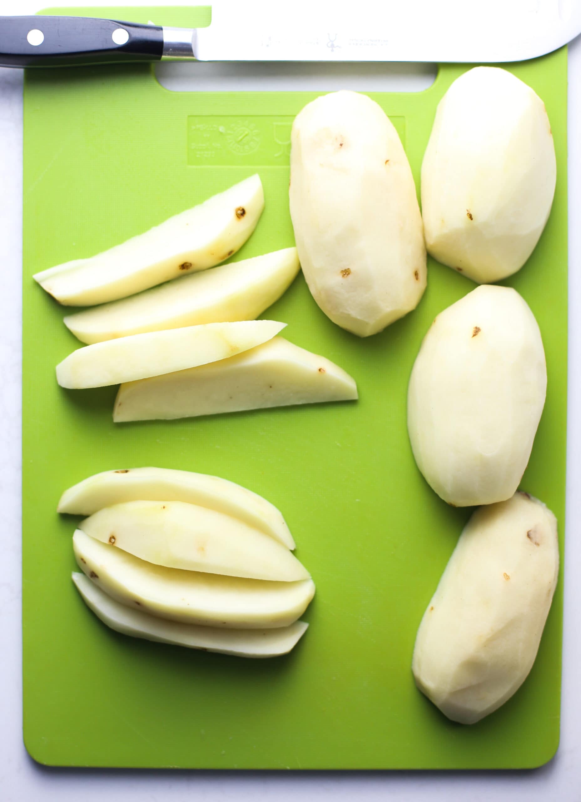 Peeled, halved, and wedged Russet potatoes on a green cutting board.