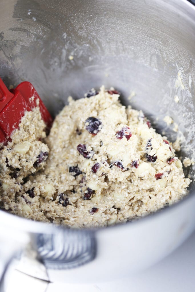 Raw white chocolate cranberry cookie batter in a large stainless steel bowl with a spatula.