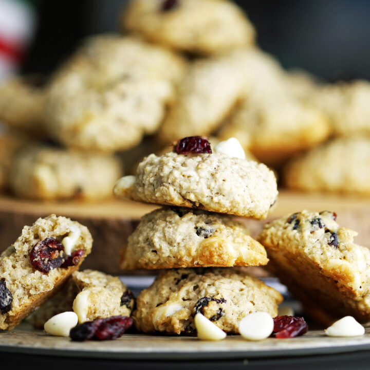 Three white chocolate cranberry oatmeal cookies on top of one another with more cookies piled high behind them.