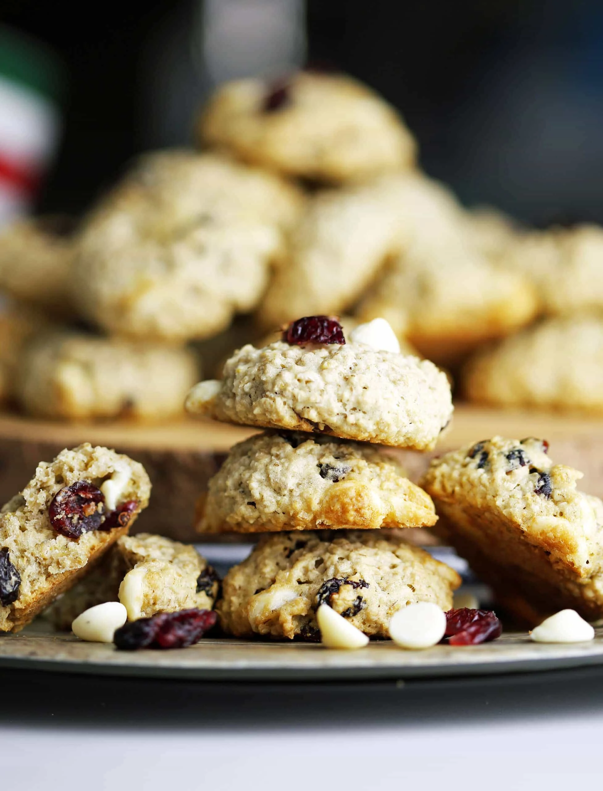 Three white chocolate cranberry oatmeal cookies on top of one another with more cookies piled high behind them.